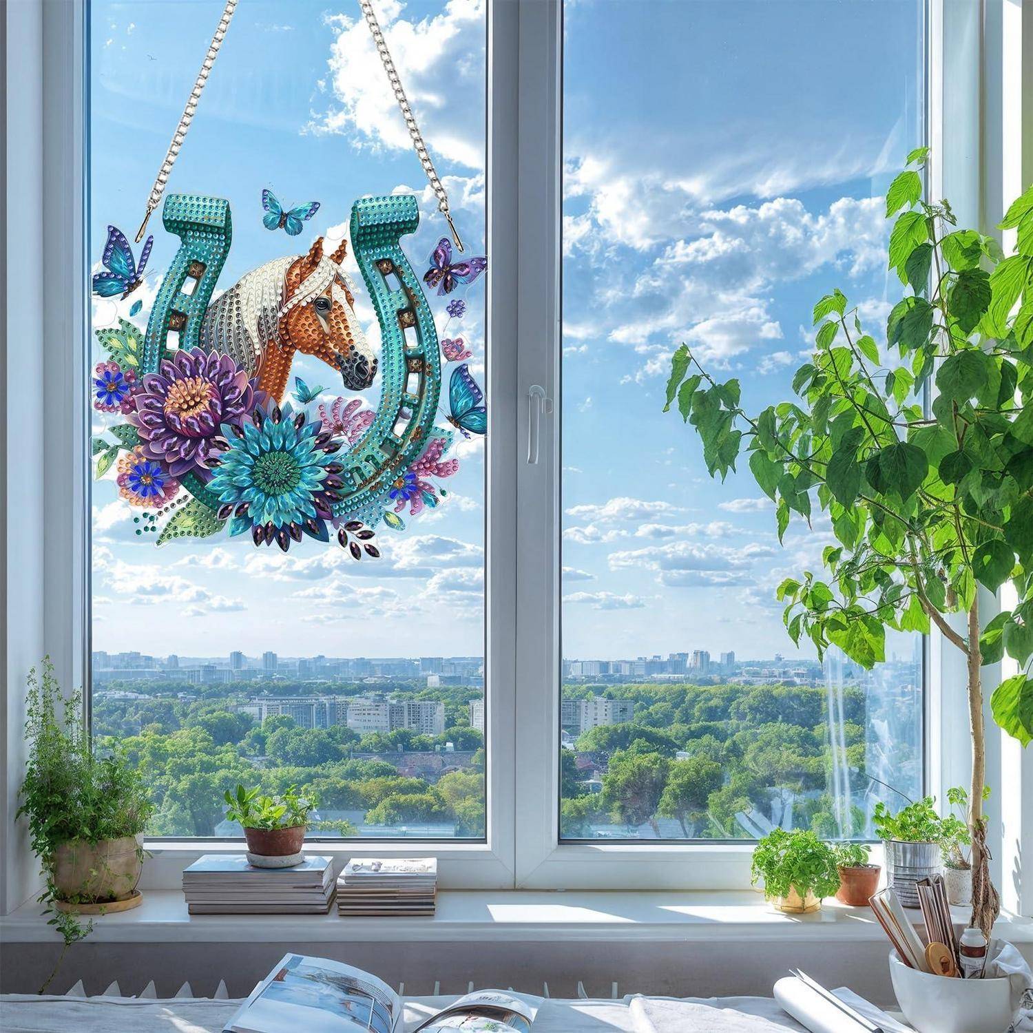 Bunte Pferde- und Hufeisen-Dekoration hängt in einem hellen Fenster über einem Stadt- und Parkblick, mit Zimmerpflanzen auf der Fensterbank.