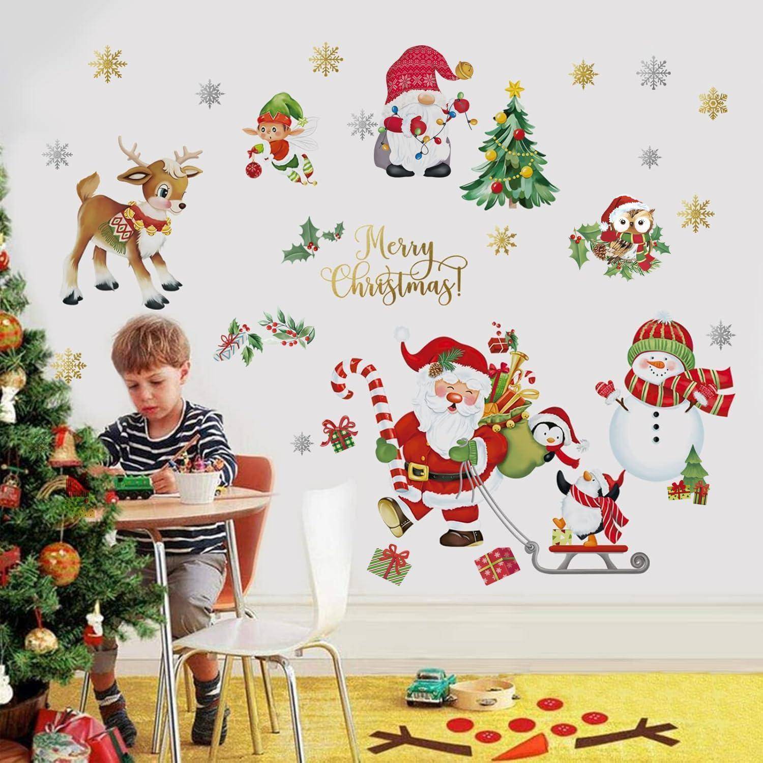 Junge, der neben einem geschmückten Weihnachtsbaum einen Spielzug baut, mit festlichen Wandtattoos einschließlich des Weihnachtsmanns, Rentieren, Schneemännern und „Frohe Weihnachten!