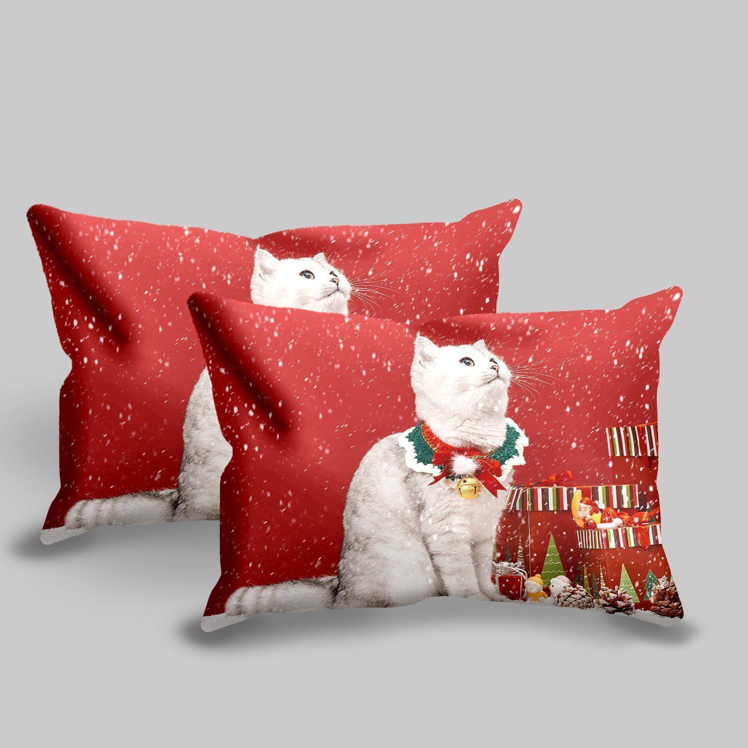Zwei rote Weihnachtskissen mit einer weißen Katzenillustration, eines zeigt die Katze in einem festlichen Halsband und einer Winterszene.