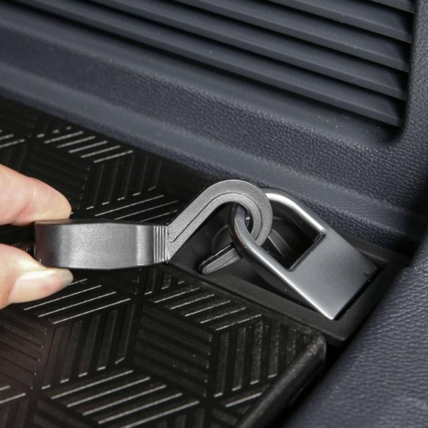 Nahaufnahme einer Hand, die einen Spannhaken an einer Metallverankerung im Kofferraum oder Ladebereich eines Autos befestigt.