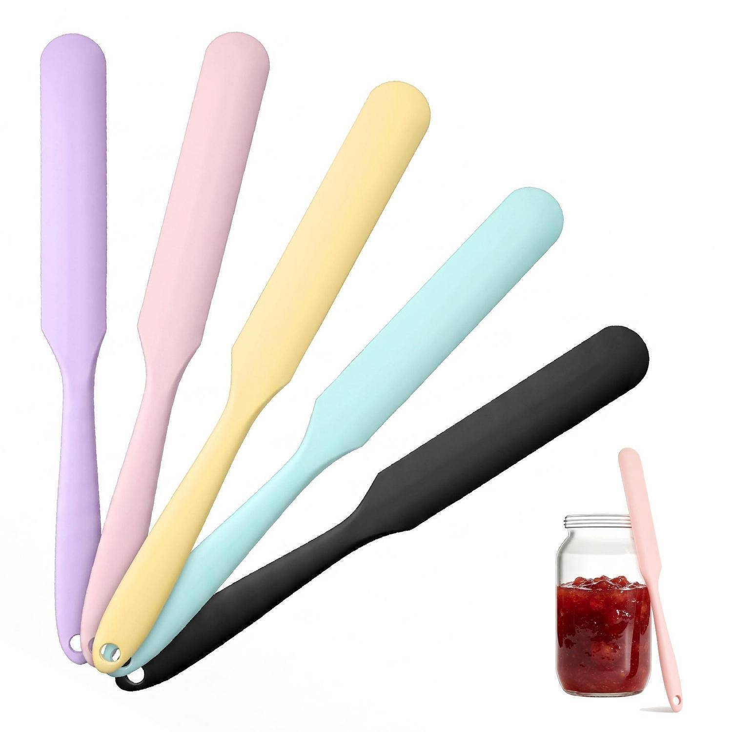 Fünf Silikonspachteln/Zuckergussspatel in Pastelltönen in Lila, Rosa, Gelb, Blau und Schwarz, gezeigt mit einem kleinen Glas roter Marmelade und einem rosa Spachtel daneben.