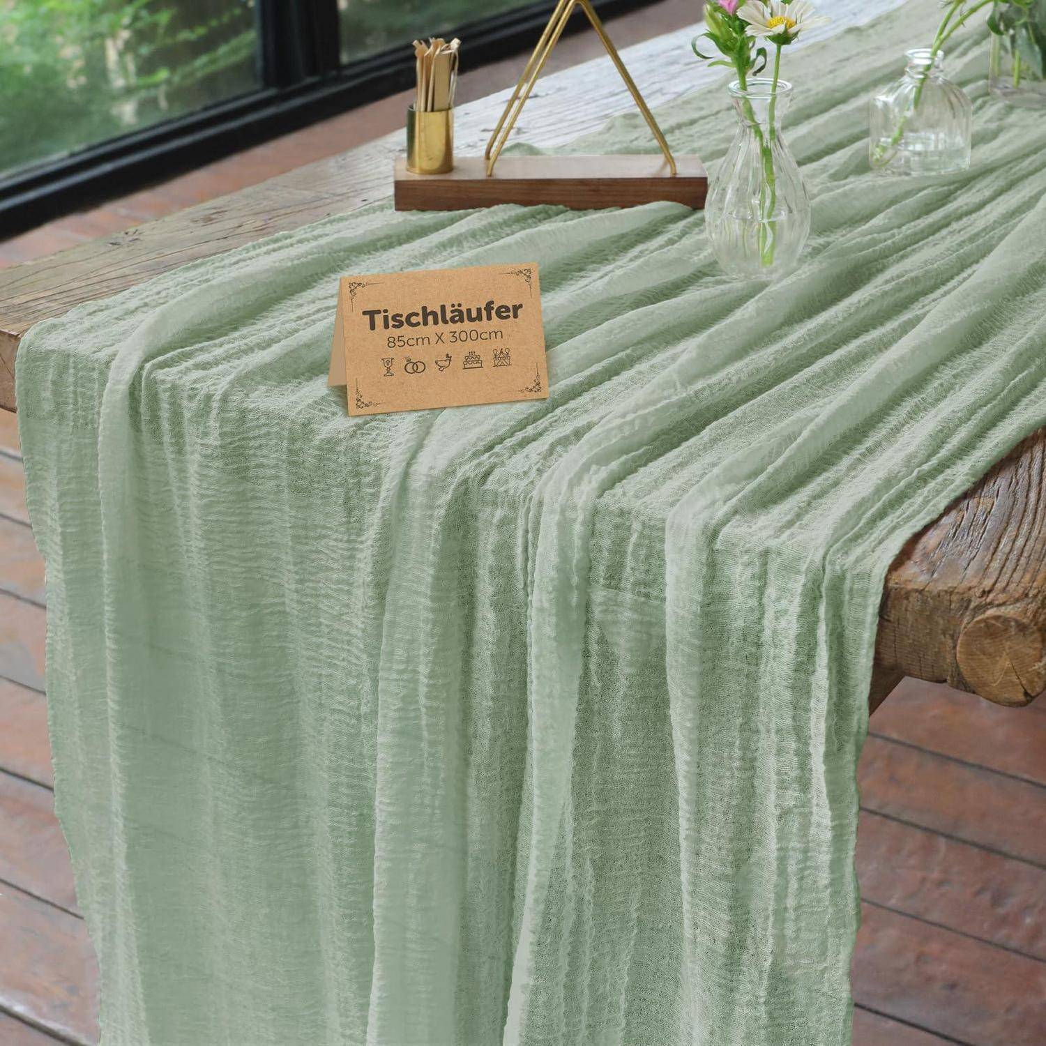 Ein blassgrüner strukturierter Tischläufer drapiert über einem Holztisch, mit einem Etikett, das „Tischläufer 85cm x 300cm