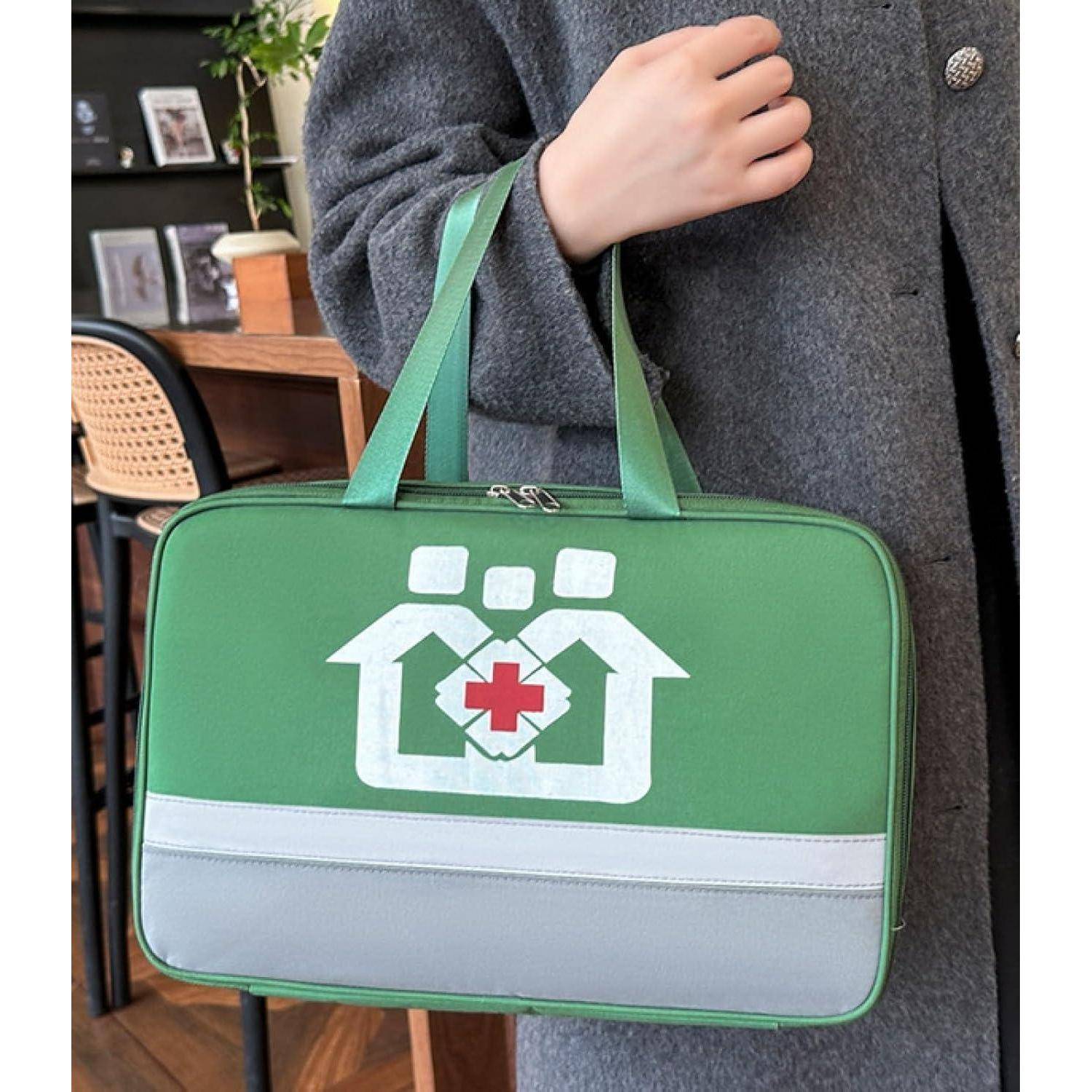 Person hält eine grüne isolierte medizinische Tasche mit einem weißen Haus-und-rotes-Kreuz-Logo und grauem Bodenpanel.