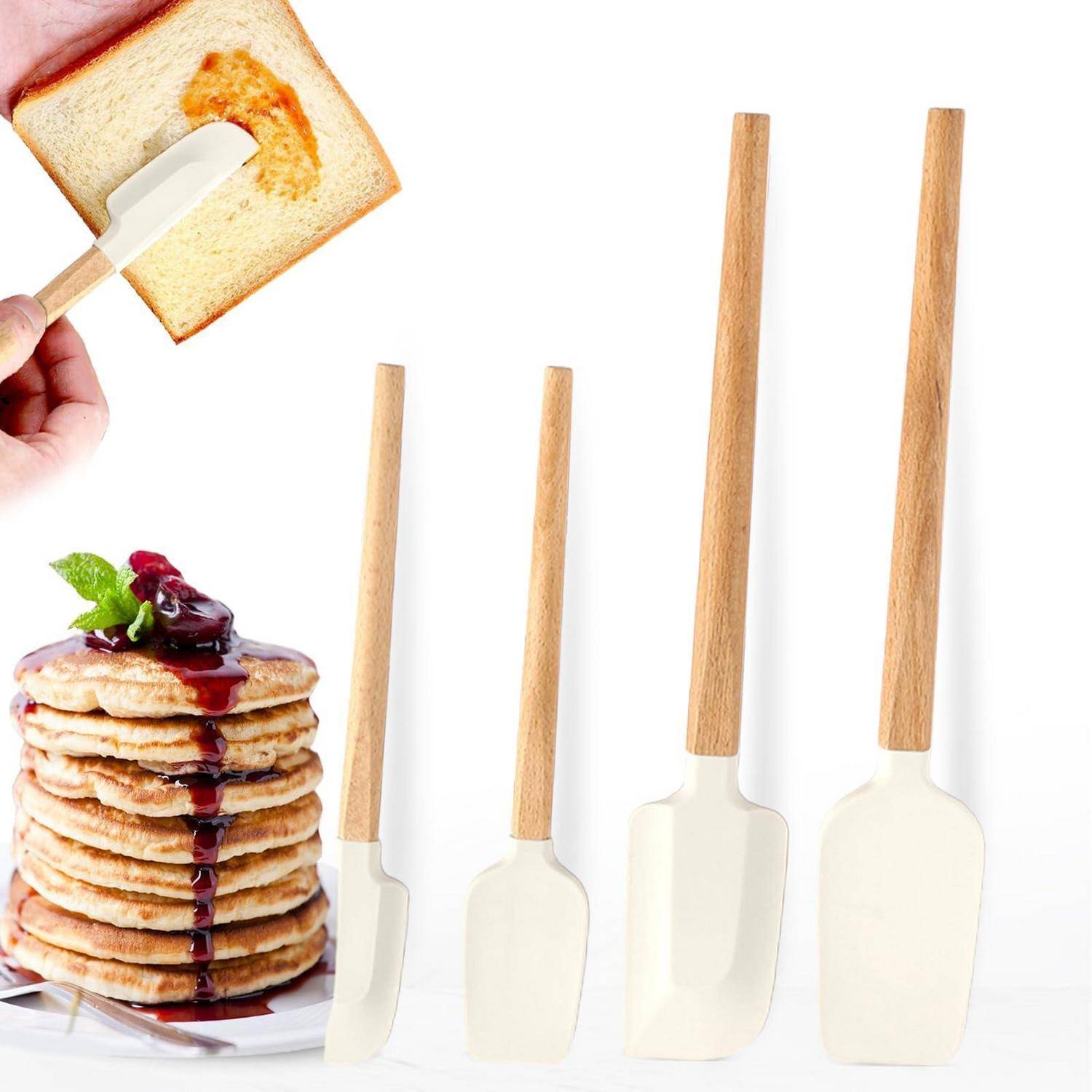 Satz von vier Silikonspachteln mit Holzgriffen und einer Hand, die Toast mit Butter bestreicht, neben einem Stapel Pfannkuchen, belegt mit Beeren auf weißem Hintergrund.