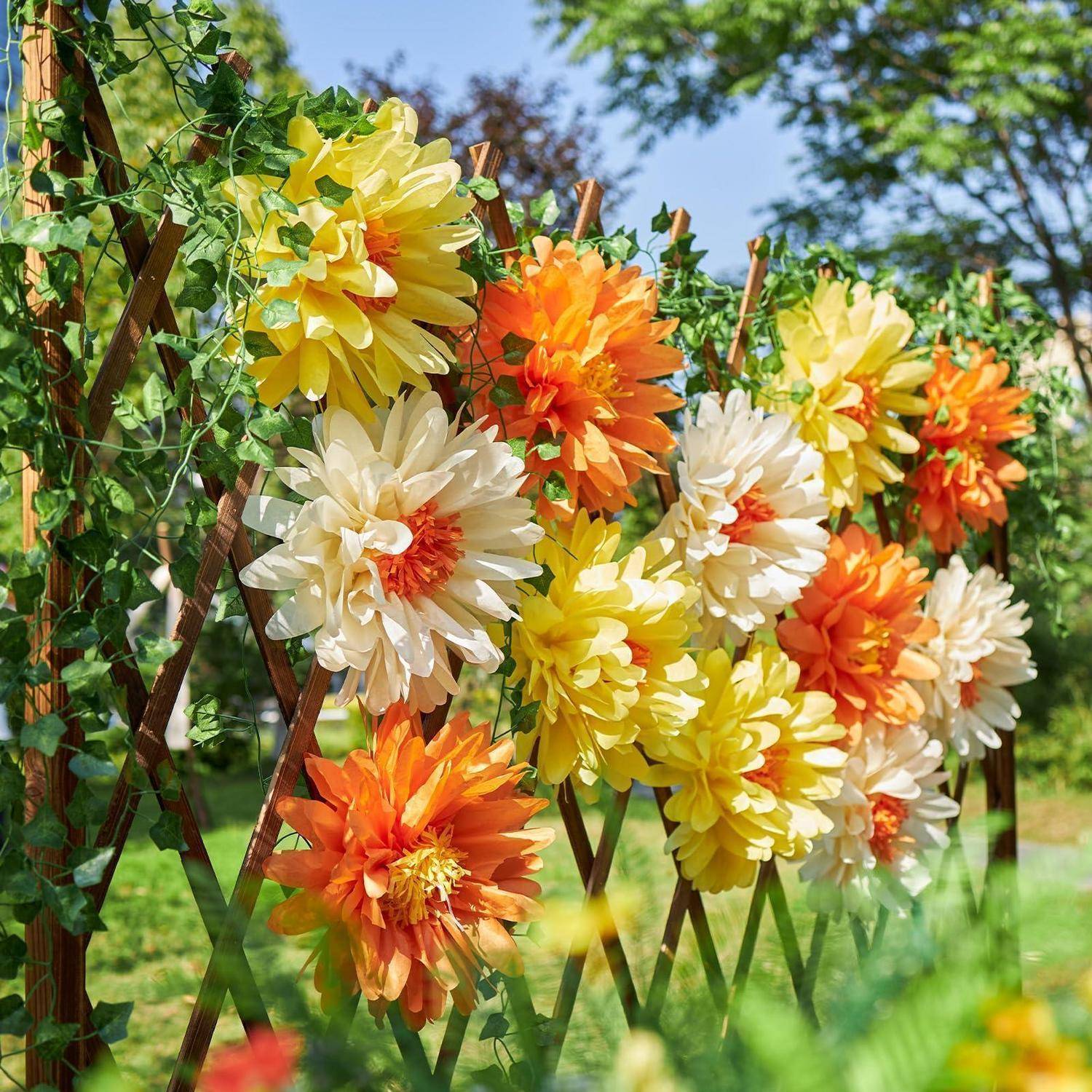 Bunte künstliche Blumen in Gelb, Orange und Weiß, die auf einem Holzgitter im Freien in einem Garten angeordnet sind.