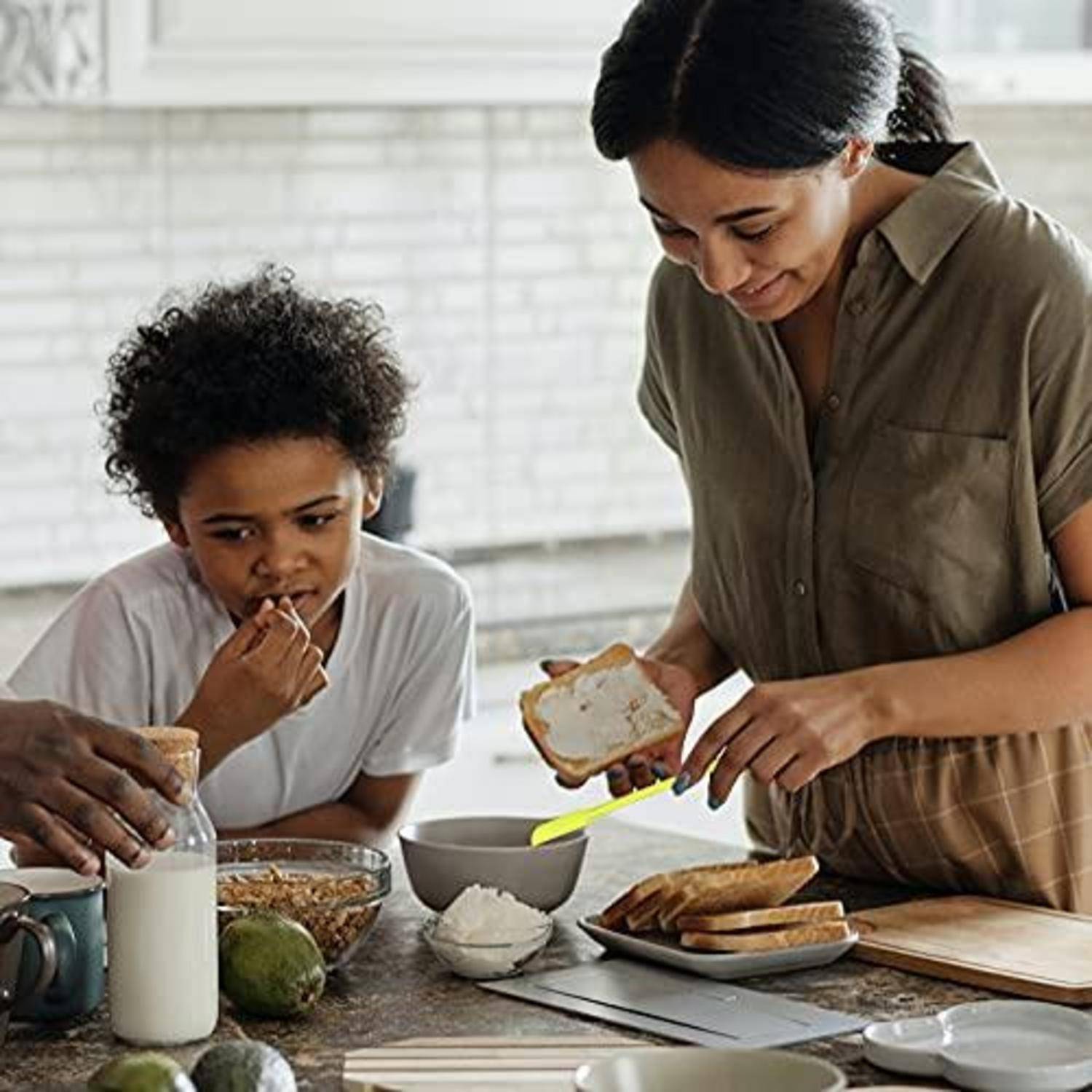 Zwei Menschen bereiten eine Mahlzeit in einer Küche zu, indem sie Lebensmittel auf Brotscheiben verteilen oder zusammenstellen, während Zutaten und Geschirr auf der Arbeitsplatte stehen.
