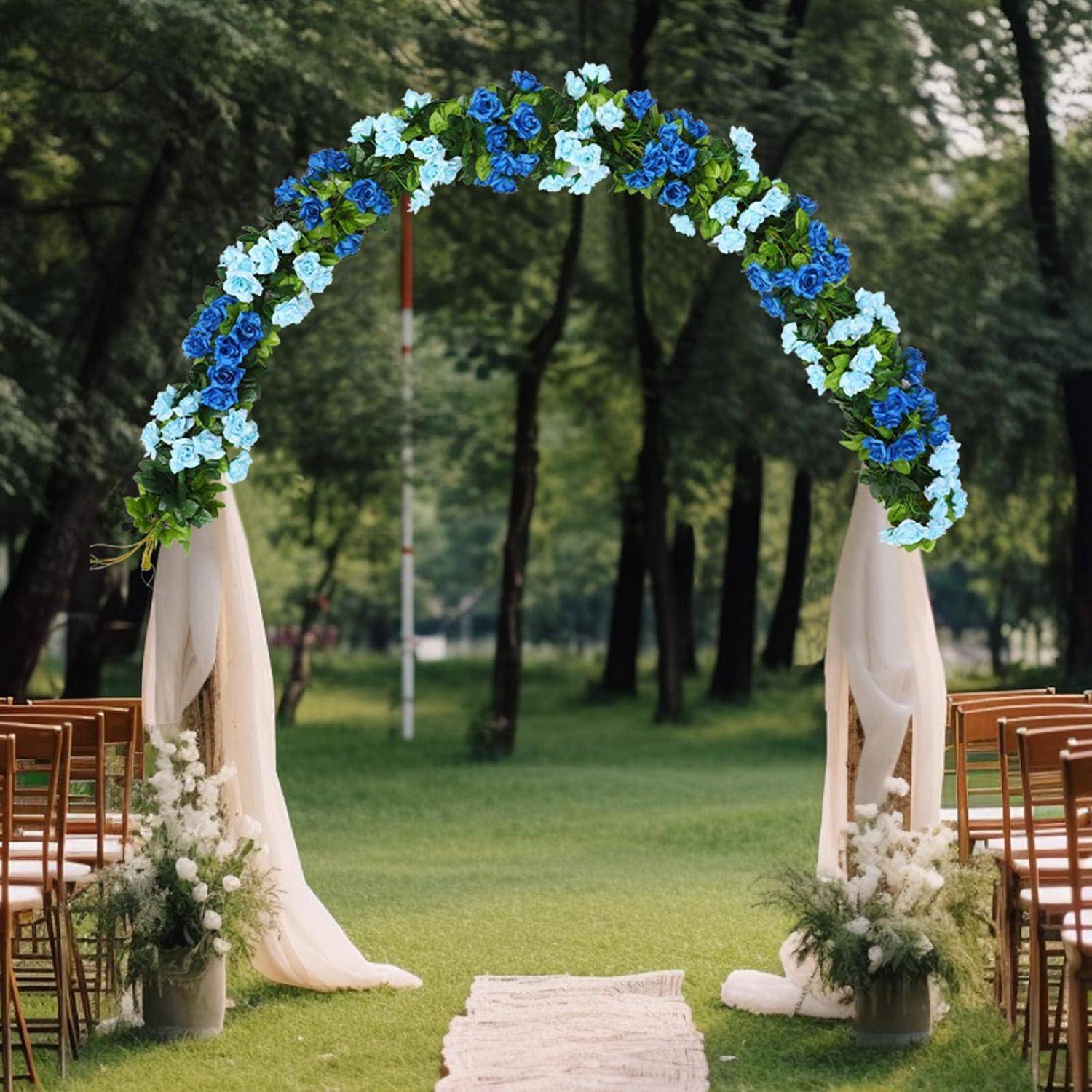 Außenhochzeitsaufbau mit einem blumen­geschmückten Bogen in Blau und Weiß, drapierte Stoffe, Läufer im Gang und Stühle auf einem grünen Rasen in einem Park.
