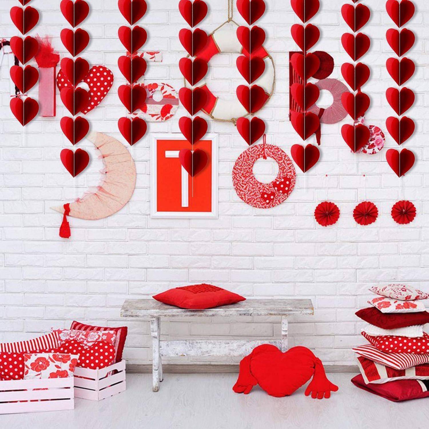 Valentinstagdisplay mit hängenden roten Herzgirlanden, dekorativen Herzformen an einer weißen Backsteinmauer und roten Kissen sowie Geschenken darunter.