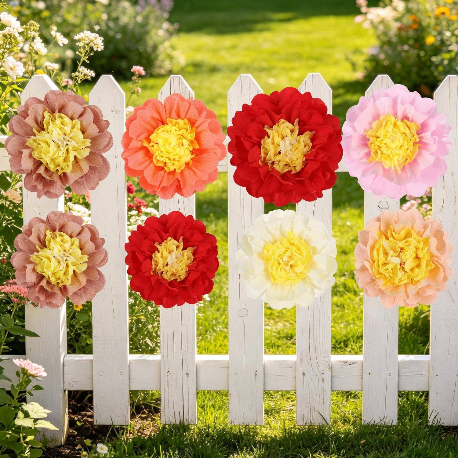Weißer Lattenzaun mit großen bunten Papierblumen in einem sonnigen Garten dekoriert.