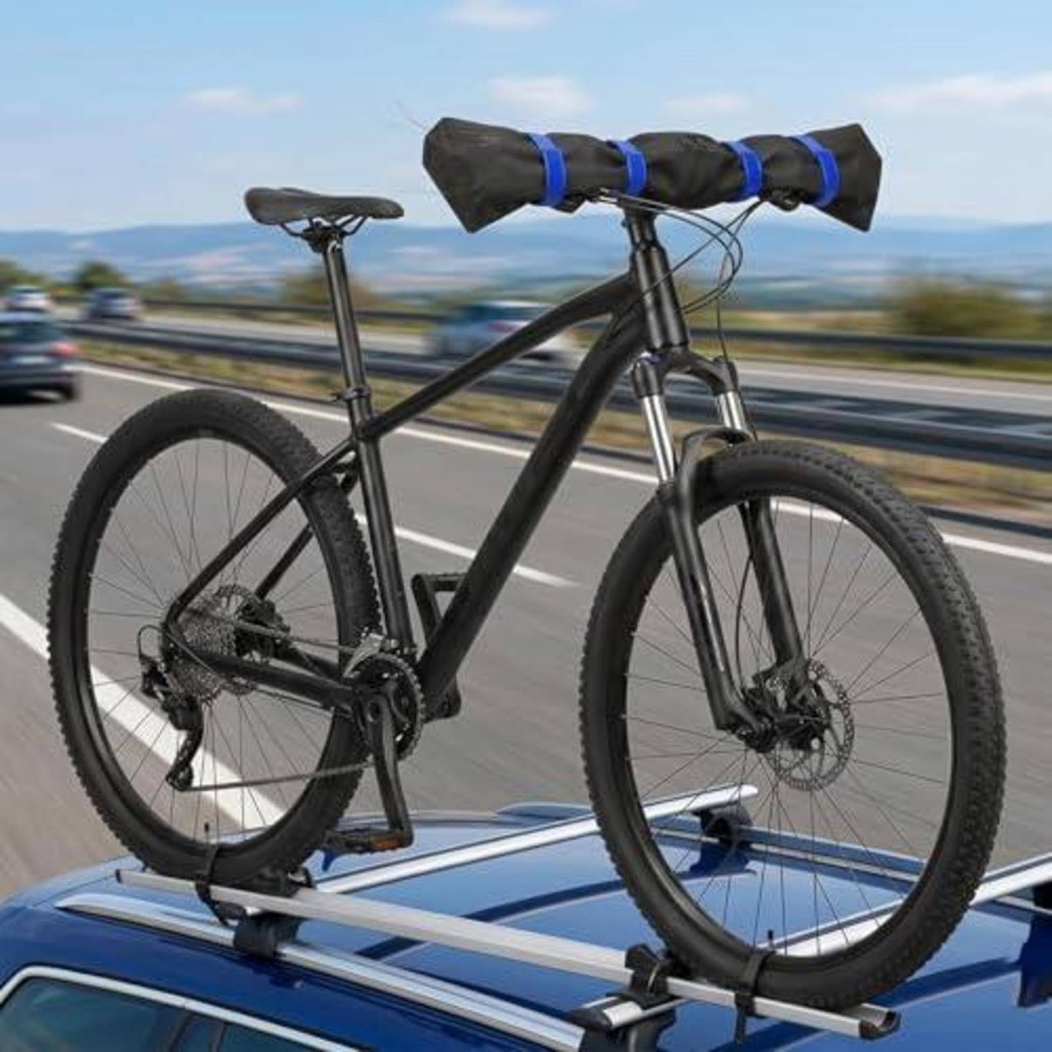Mountainbike auf einem Dachträger eines Autos gesichert mit einem aufgerollten Schlafsack, der auf dem Oberrohr befestigt ist, während das Auto auf einer Autobahn fährt.