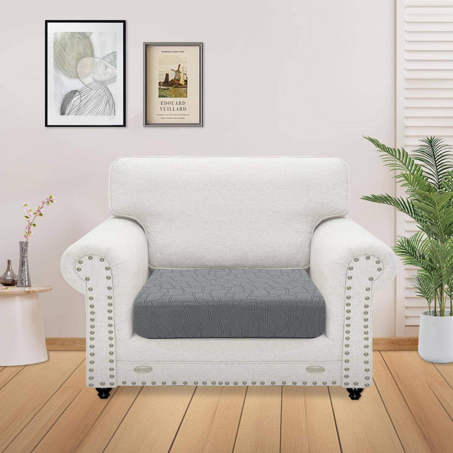 Cremefarbener gepolsterter Sessel mit grauem Sitzkissen in einem hellen Wohnzimmer, flankiert von Wandkunst und Topfpflanzen.