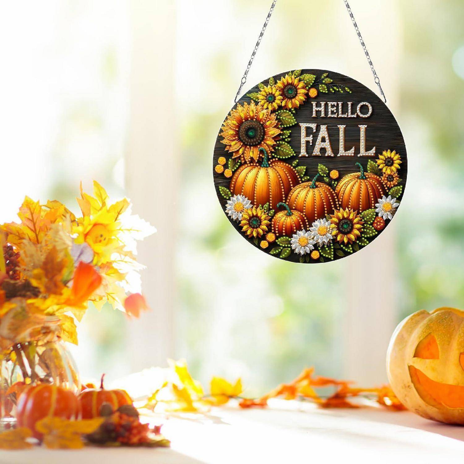 Hängendes rundes Schild mit Kürbissen und Sonnenblumen mit der Aufschrift „HELLO FALL", gezeigt in einer hellen Herbst-Wohndekorationsszene mit Blumen und einem geschnitzten Kürbis.