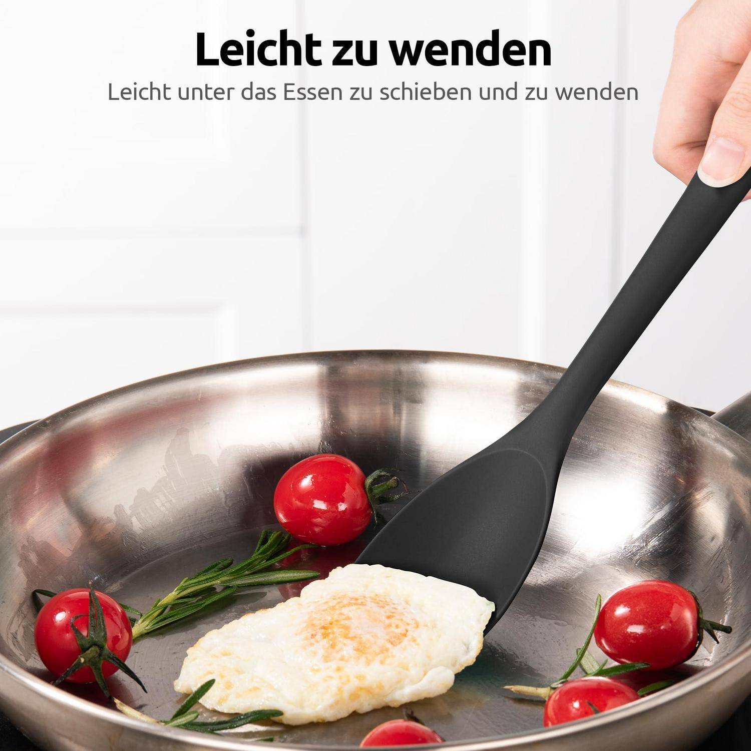 Schwarzer Silikonspatel, der ein Spiegelei in einer Edelstahlpfanne mit Kirschtomaten und Kräutern wendet; Deutscher Text besagt „Leicht zu wenden