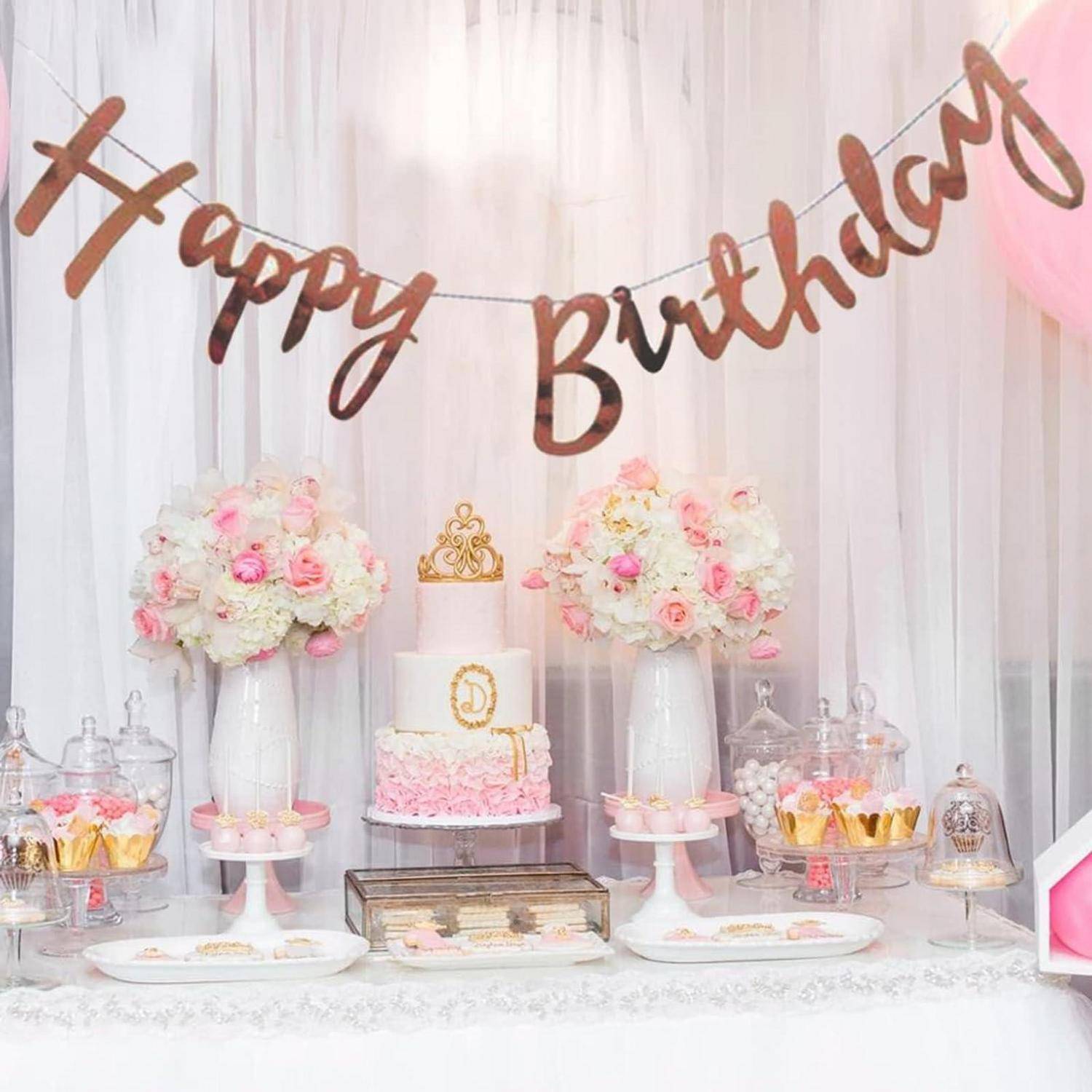 Geburtstagsdesserttisch mit rosa-weißen Blumendekorationen, einer gestuften Torte und einem „Alles Gute zum Geburtstag