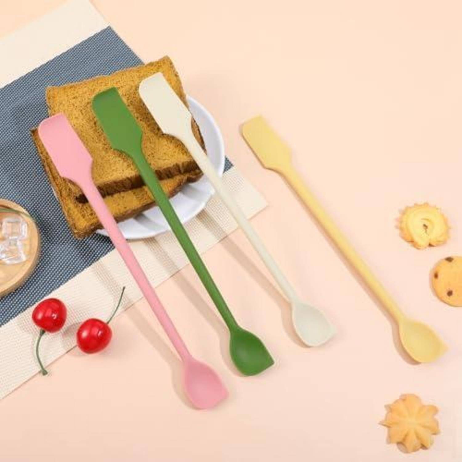 Vier bunte Kuchenspatel mit langen Griffen oder Löffel-Spatel, die um ein Stück Kuchen auf einem Teller angeordnet sind, dargestellt als Küchenutensilien auf pastellfarbenem Hintergrund.