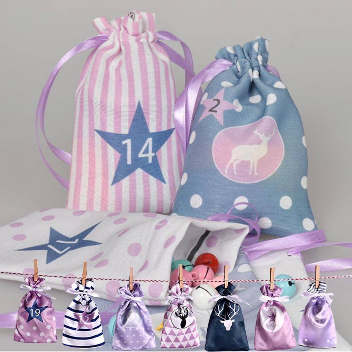 Geschenktüten und Kordelzugbeutel in Rosa und Blau, verziert mit Sternen, Hirsche und Nummernaufklebern, was auf ein Advents- oder Countdown-Set hindeutet.