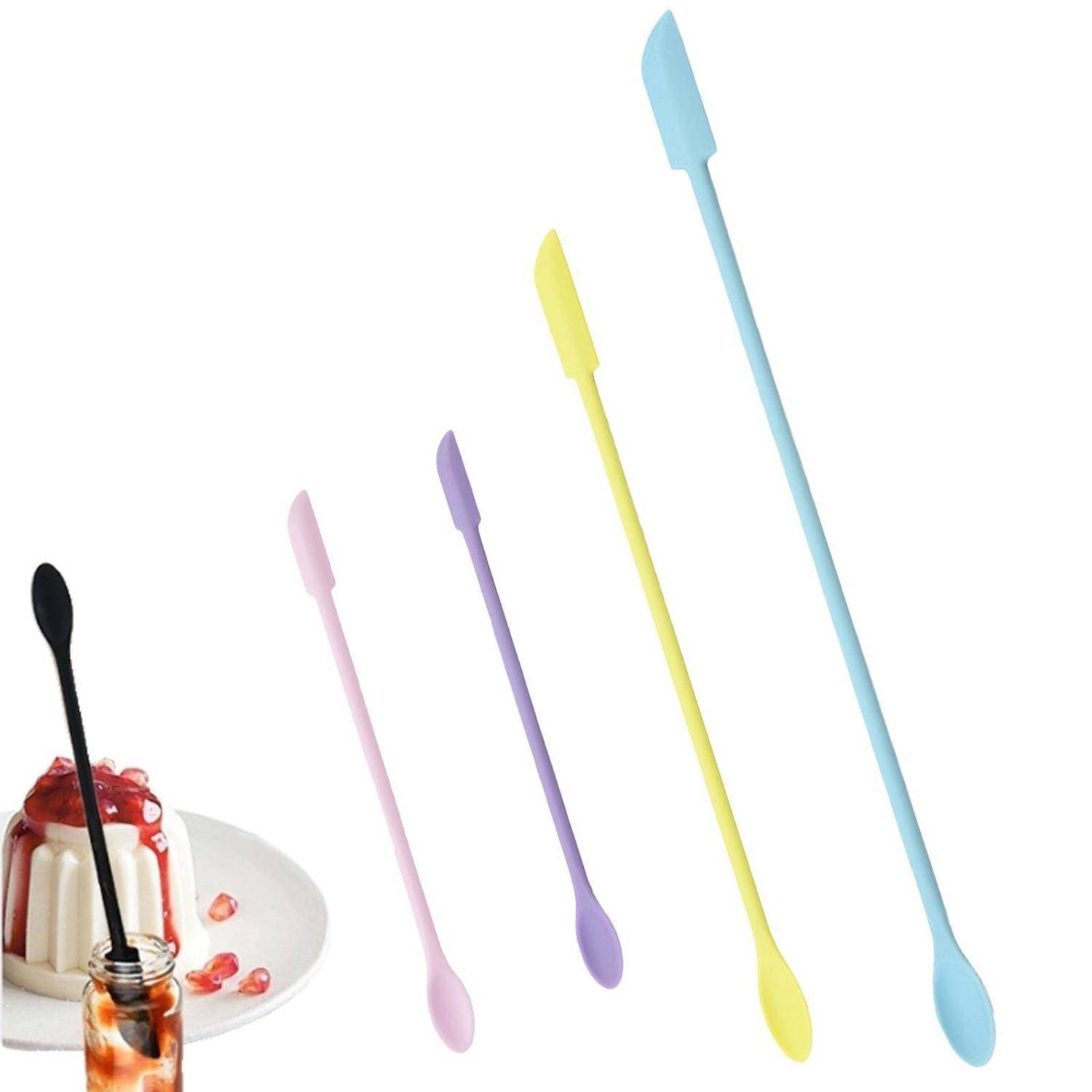 Fünf lange bunte Rührlöffel oder Spatel aufrecht neben einem Dessert in einem Glaskrug auf weißem Hintergrund angeordnet.