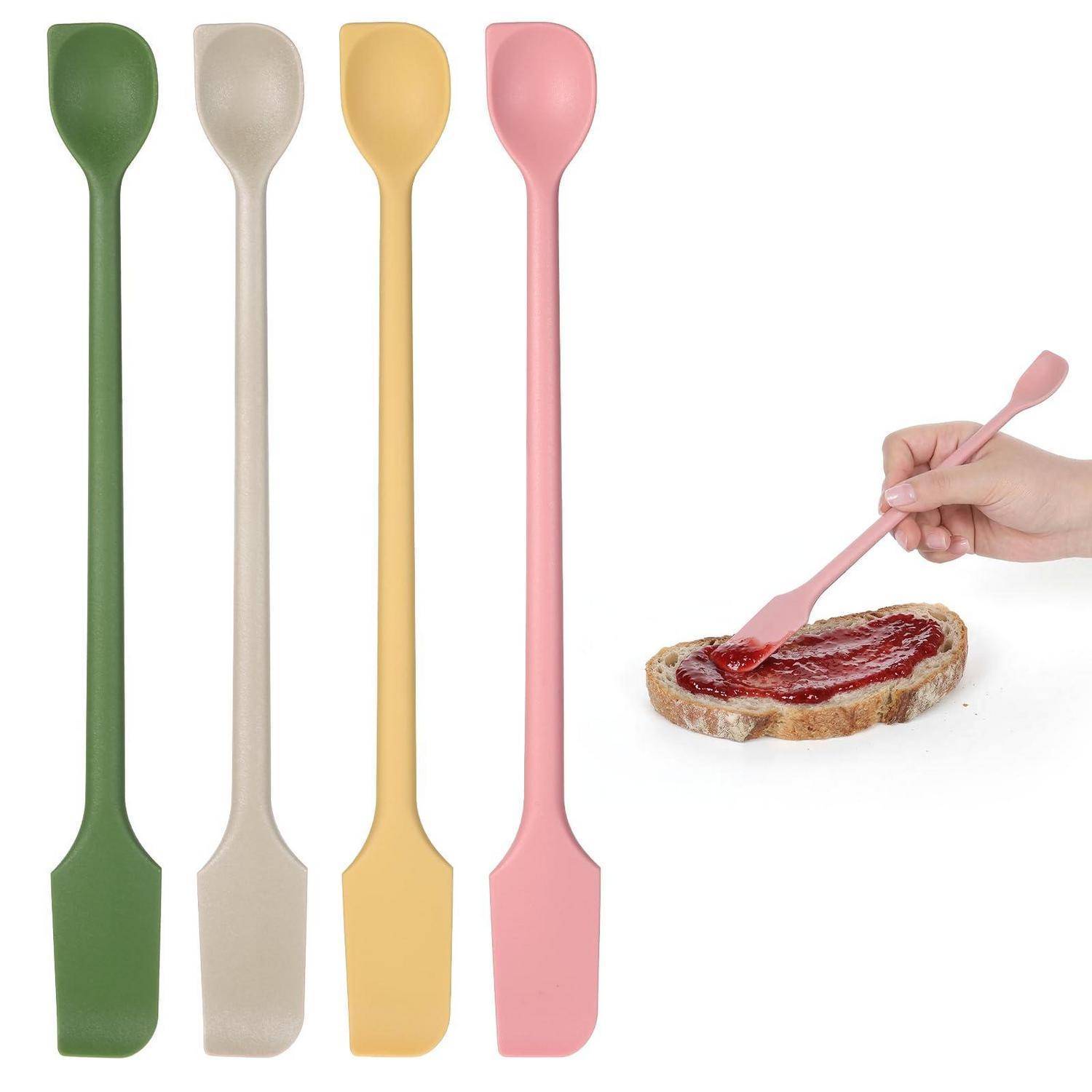 Satz von vier langen Silikonspachteln in Grün, Beige, Gelb und Rosa; eine Hand benutzt einen rosa Spachtel, um Marmelade auf Brot zu streichen.