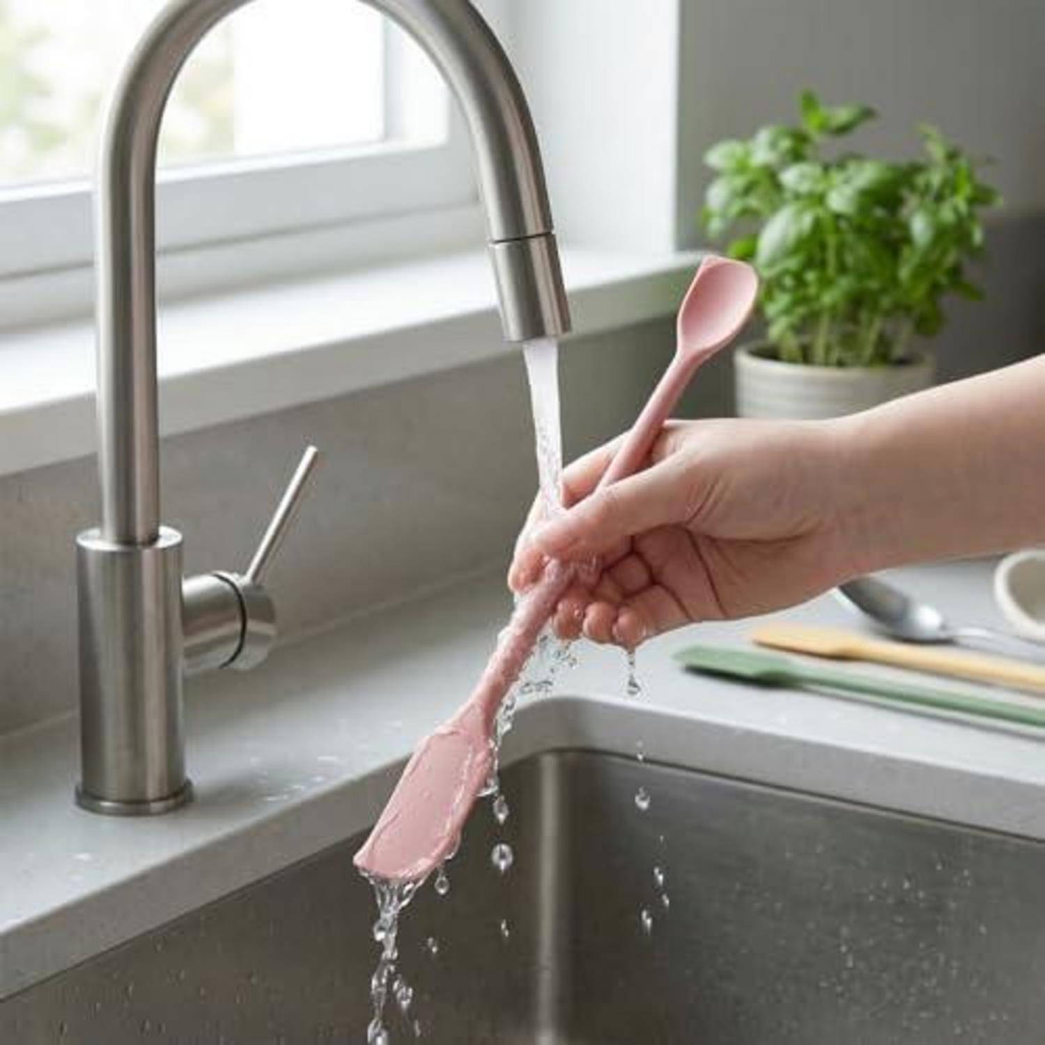 Einen rosa Spatel unter einem laufenden Wasserhahn in der Küche neben einem Spülbecken von Hand waschen