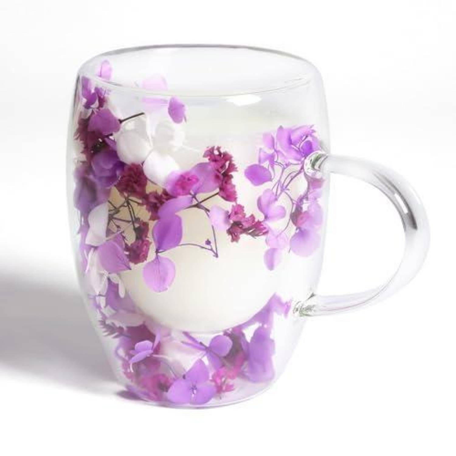Klares Glaskrug, verziert mit lila und weißen Blumen, gefüllt mit einer weißen Kerze oder Wachs