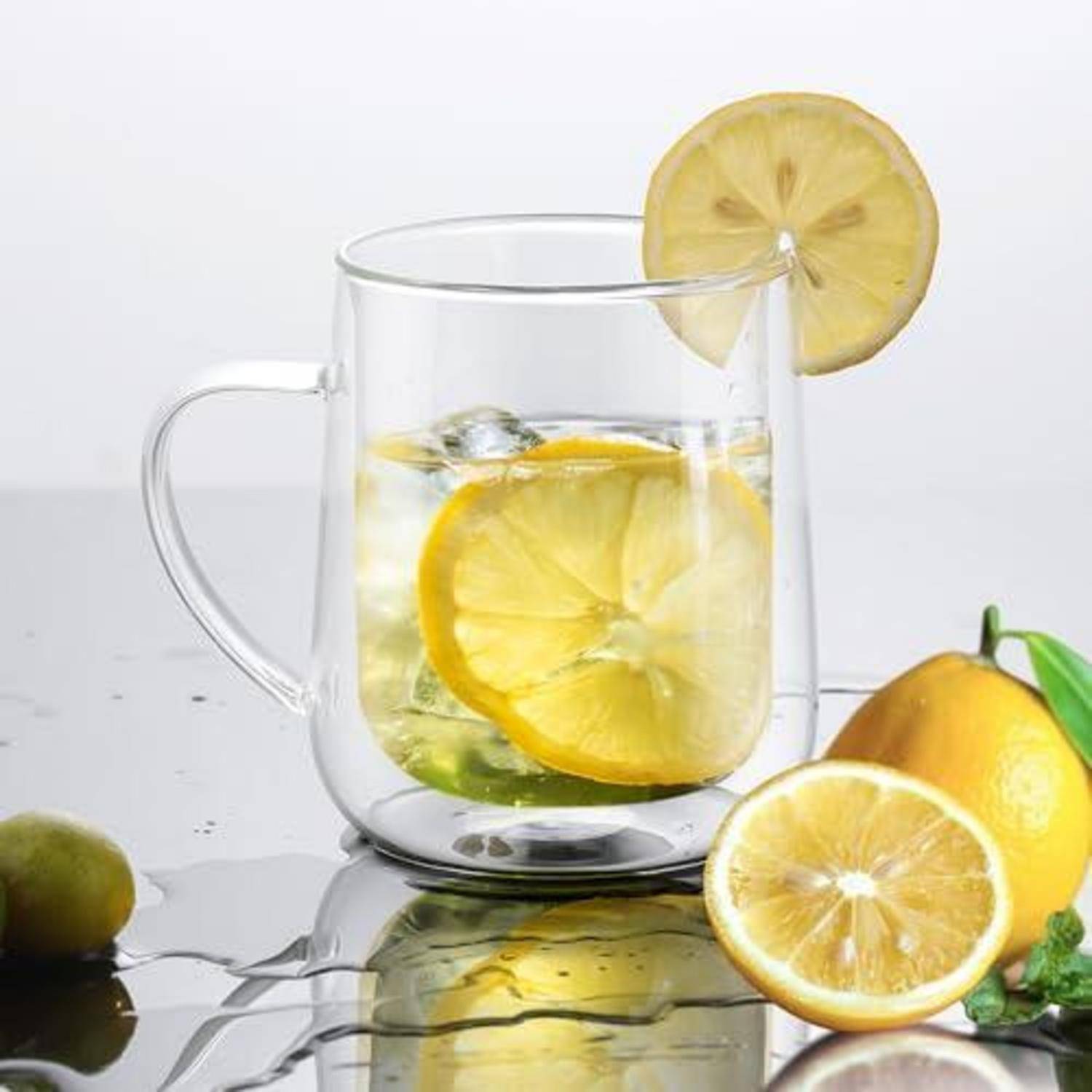 Glastasse mit Zitronenwasser mit Eis, Zitronenscheiben und einer Zitrongarnitur auf weißem Hintergrund.