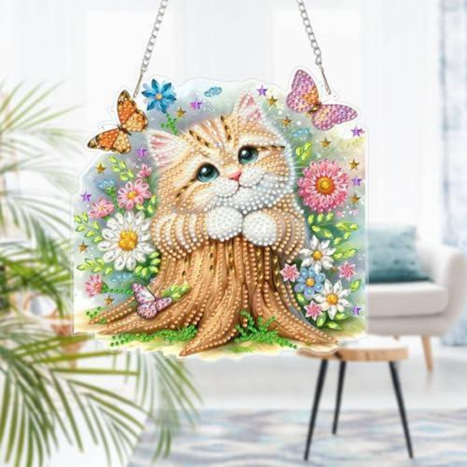 Dekoratives Hängekunstwerk eines flauschigen Kätzchens, das aus einem Baumstumpf lugt, umgeben von Blumen und Schmetterlingen.