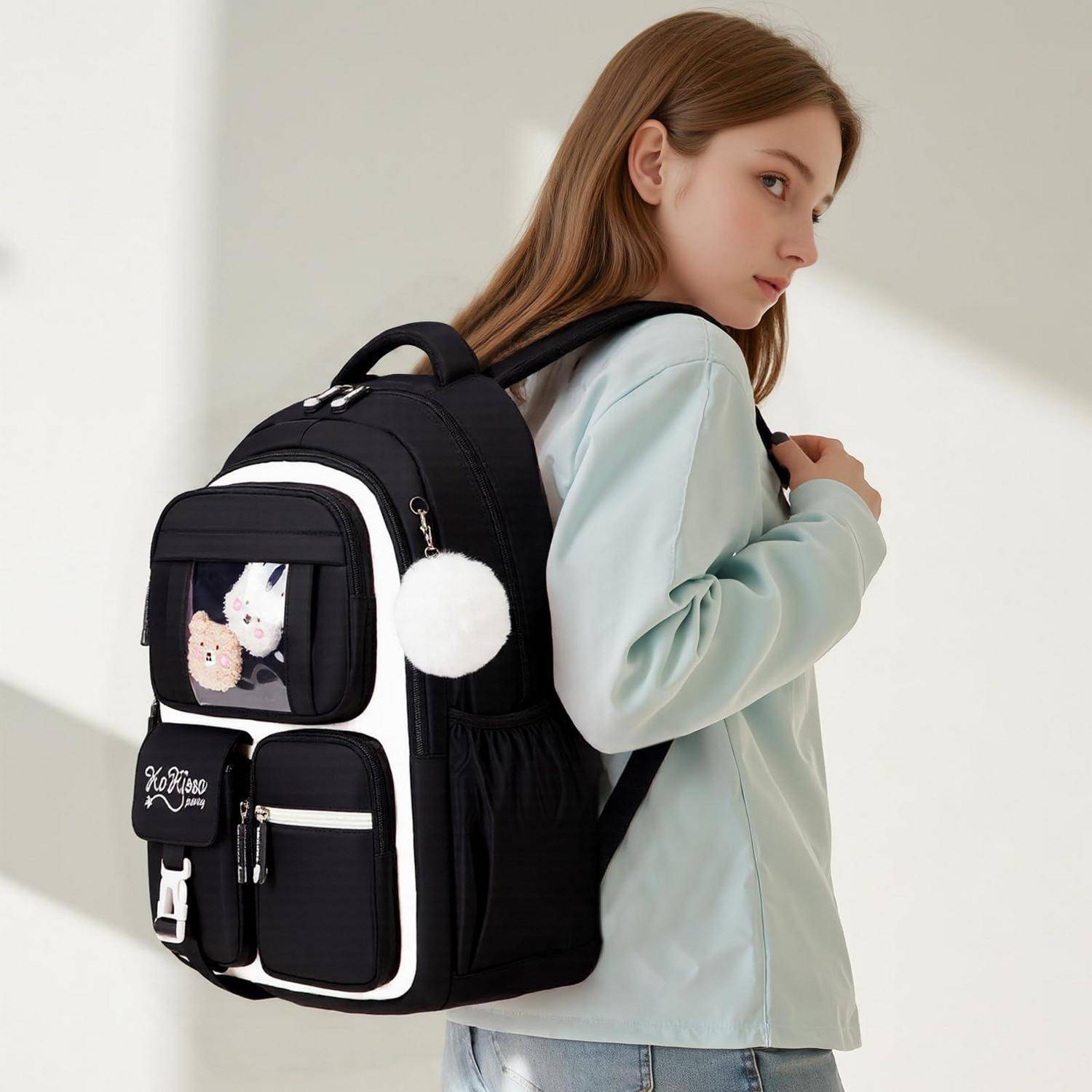 Junge Frau, die einen schwarzen Rucksack mit weißer Borte trägt, mehrere Reißverschlusstaschen und eine transparente Display-Tasche mit Plüsch-Anhängern, von der Seite in Innenräumen gezeigt.
