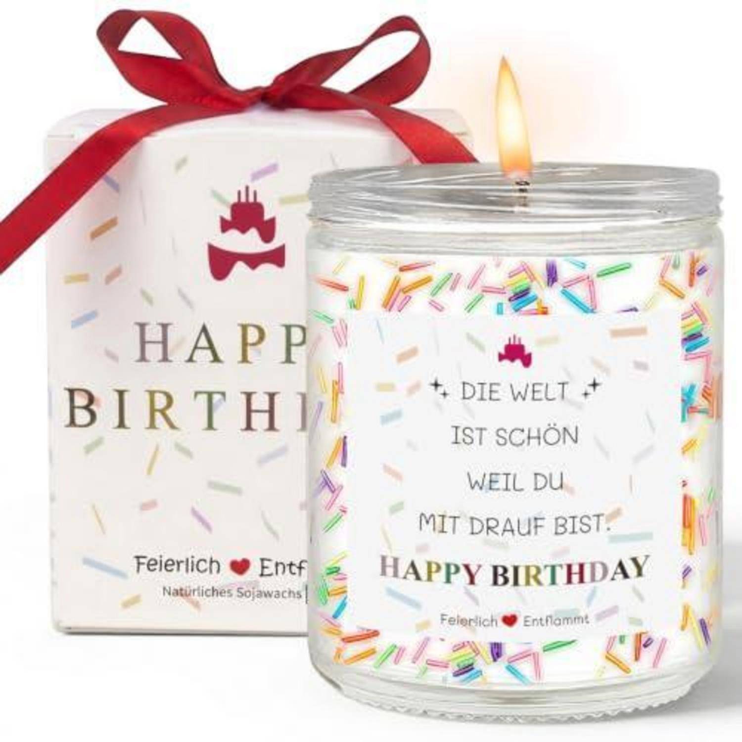 Brennende Geburtstagskerze in einem Glaskrug mit Regenbogen-Streuseln und deutschem/englischem "Happy Birthday""-Text, gezeigt mit passendem Geschenkkarton und rotem Band.