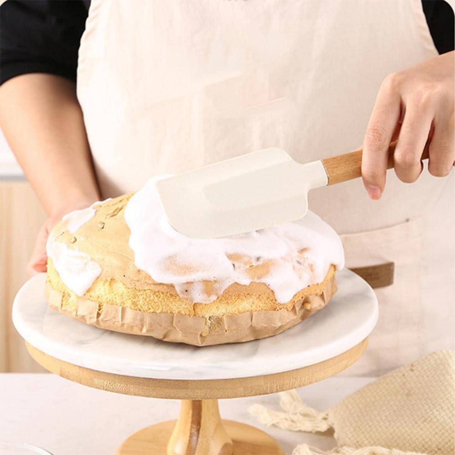 Eine Person verziert einen Schwammkuchen auf einem Drehteller mit einem Spachtel in einer Küche.
