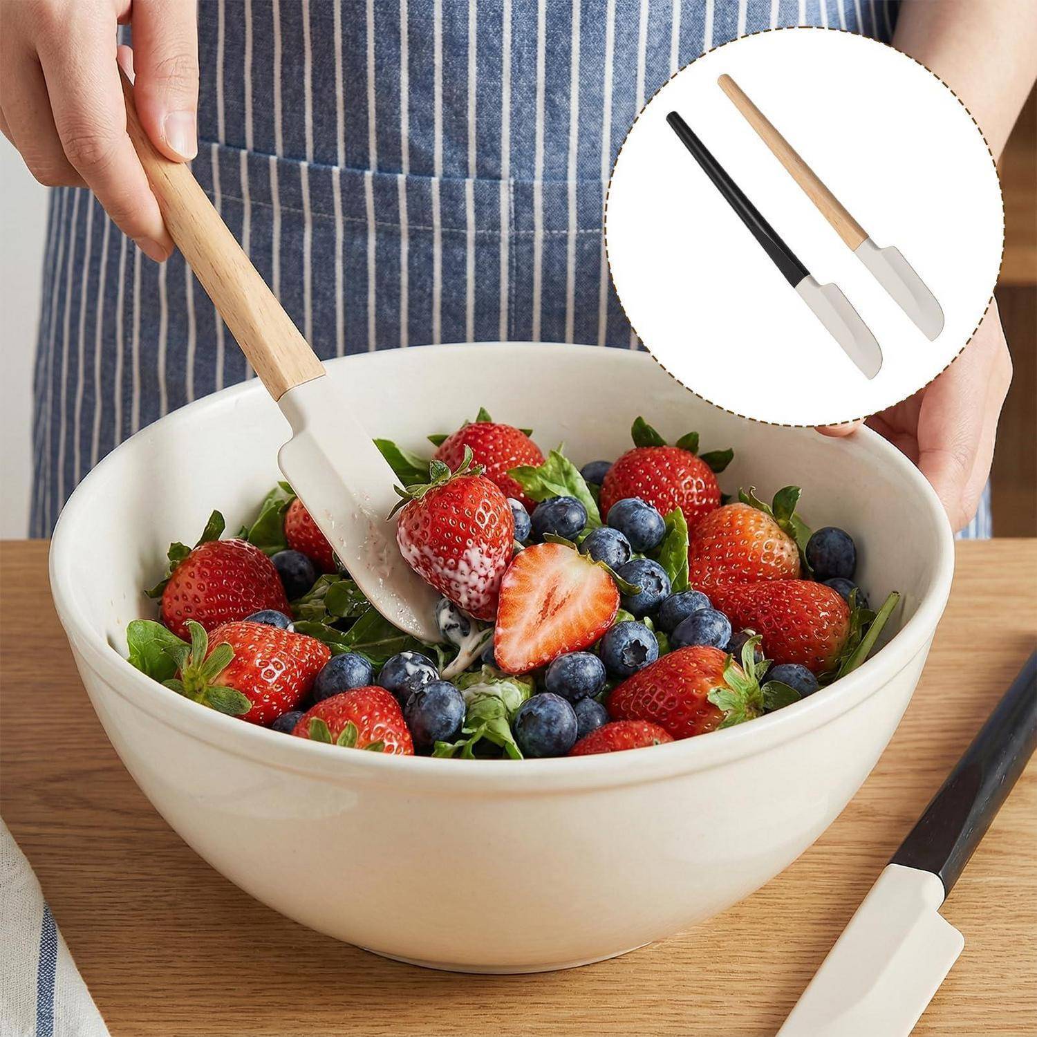 Person, die eine Schüssel mit Erdbeeren und Blaubeeren mit einem Silikonspatel mischt; die Einfügung zeigt zwei Spatel, schwarz und beige, auf weißem Hintergrund.