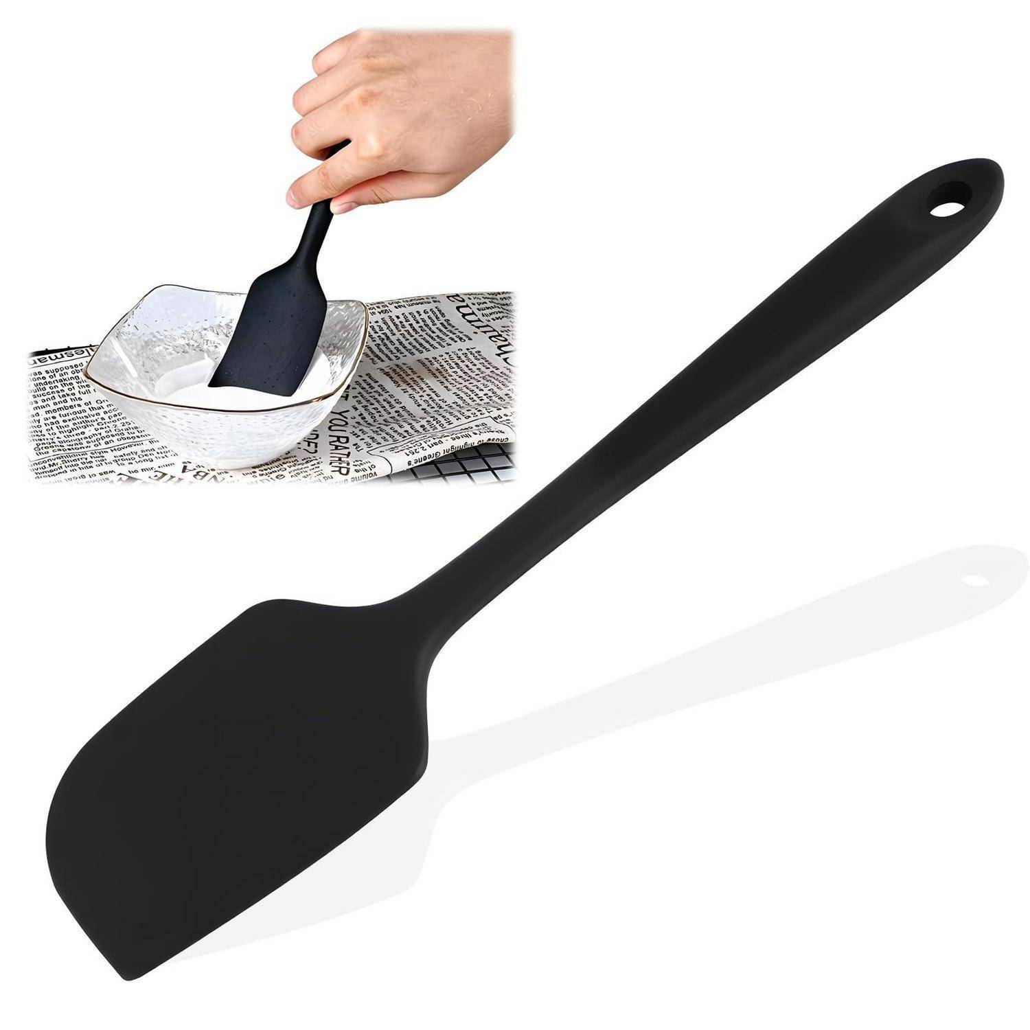 Großflächig auf weißem Hintergrund gezeigte schwarze Silikonspachtel mit eingefügtem Bild einer Hand, die mit einer Schüssel auf einer Zeitung rührt, was auf die Verwendung zum Mischen oder Backen von Lebensmitteln hindeutet.