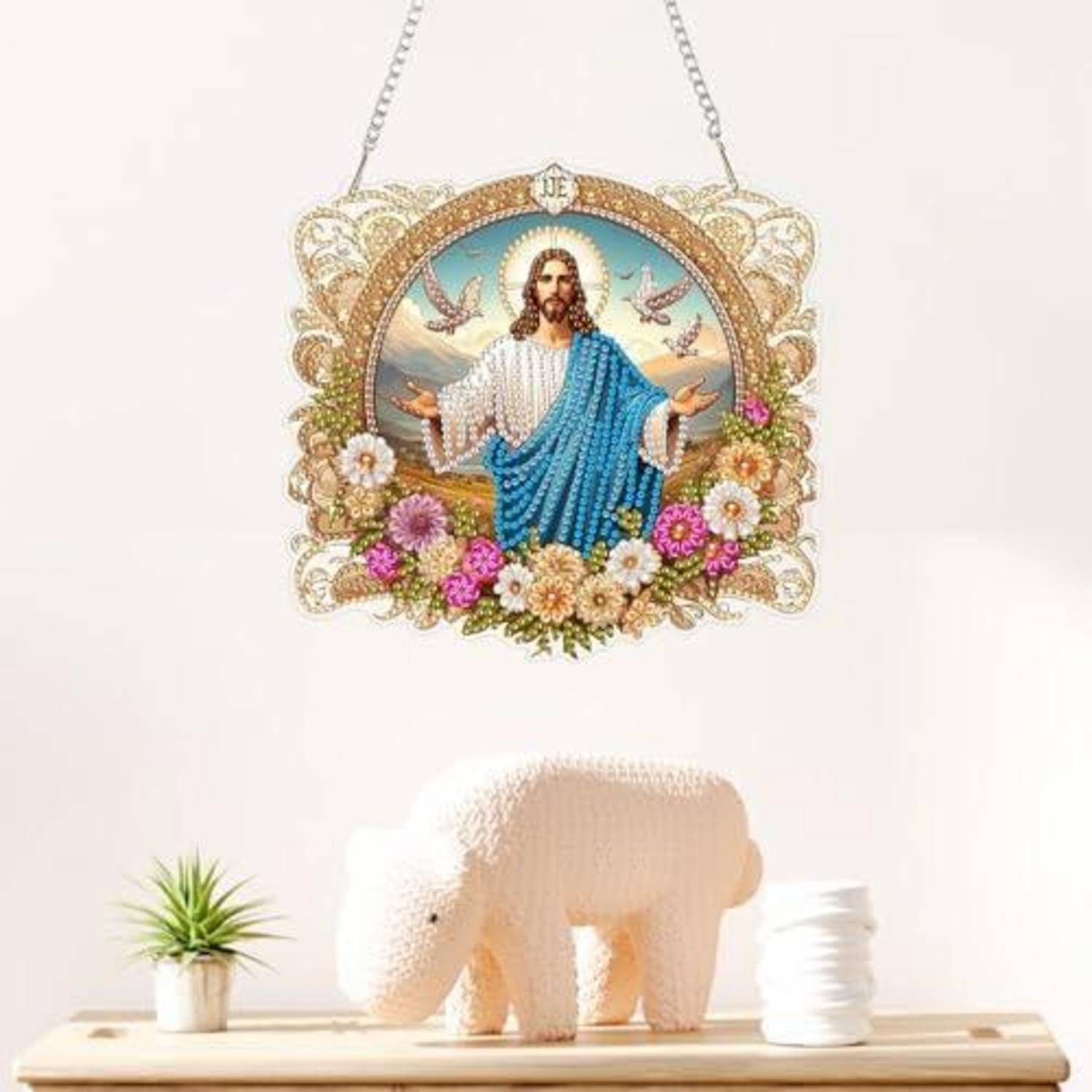 Dekorative Wandbehang mit Jesus und Blumen sowie Vögeln über einer weißen Elefantenskulptur auf einem Holzregal mit einer kleinen Topfpflanze und gestapelten weißen Tellern.