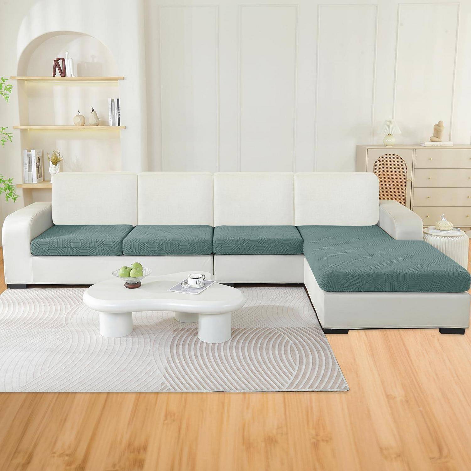 Modernes Wohnzimmer mit einer weiß-türkisfarbenen Eckgarnitur, rundem Couchtisch, hellem Holzregal und Kommode sowie einem gemusterten Teppich.