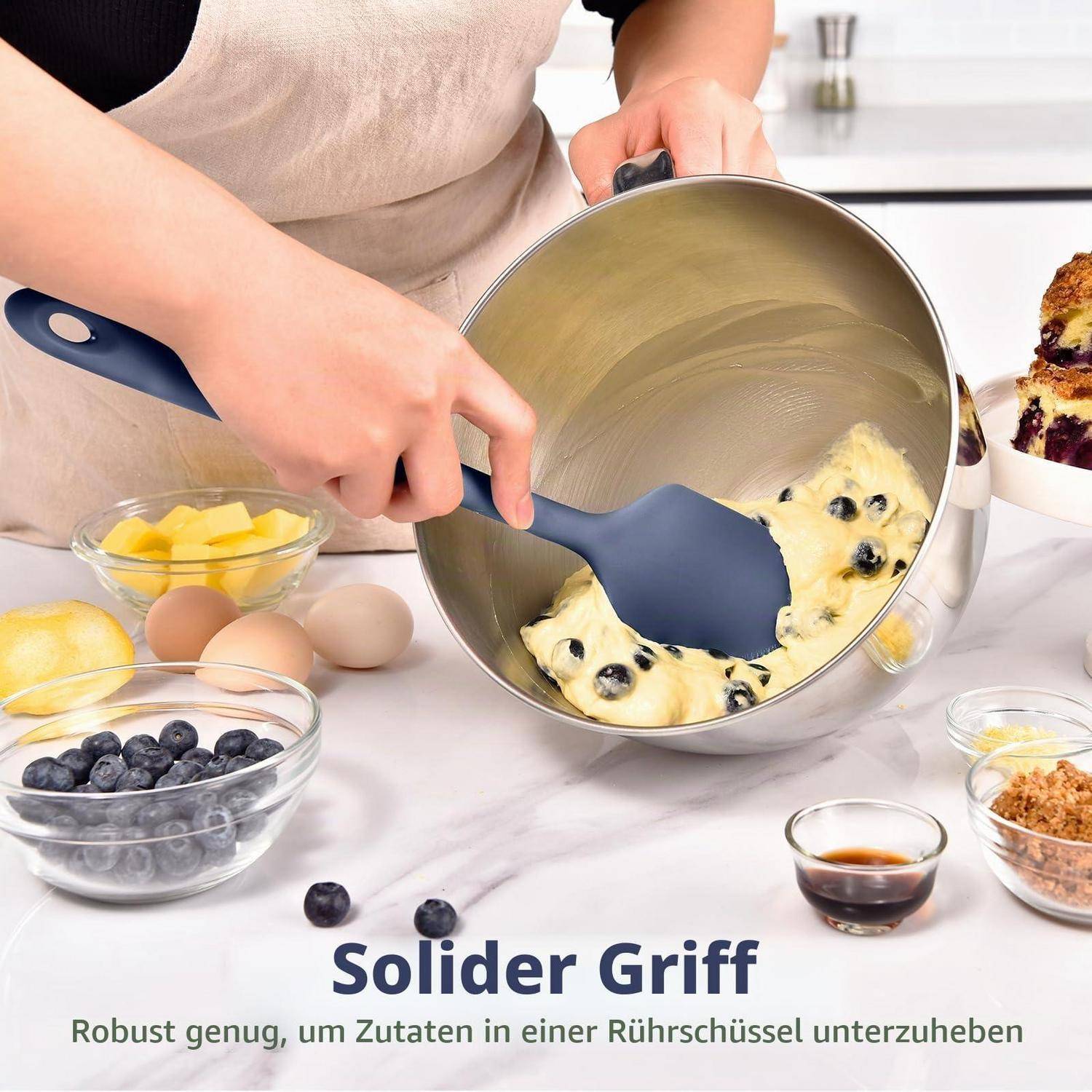 Person benutzt einen blauen Silikonspatel, um Blaubeeren in einen Teig in einer Rührschüssel zu falten, mit Zutaten auf der Arbeitsplatte und deutschem Text „Solider Griff