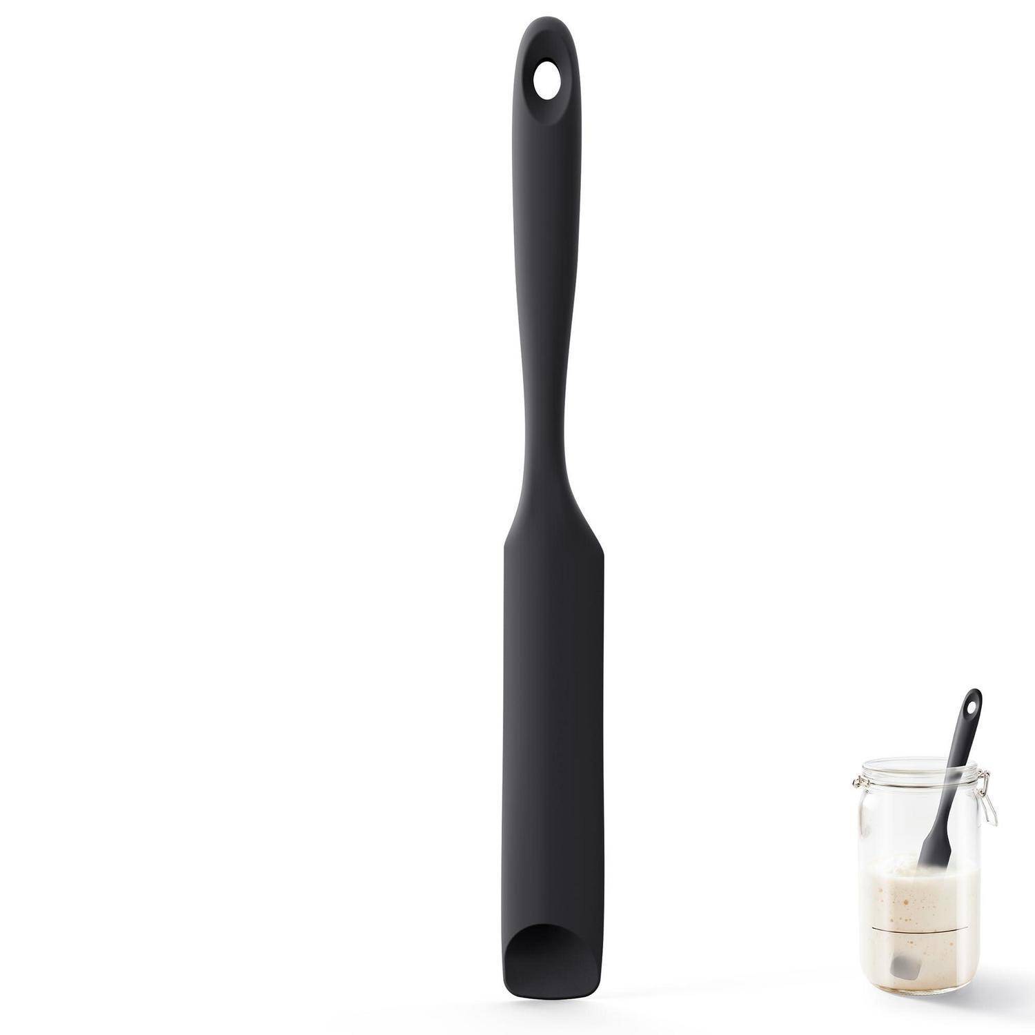 Schwarzer Silikonspatel mit Aufhängeloch, aufrecht auf weißem Hintergrund dargestellt, mit einem kleinen Behälter mit Teig und Spatel-Ausschnitt unten rechts.