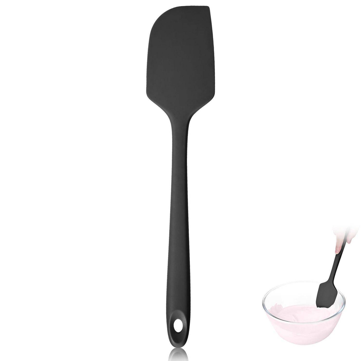 Schwarzer Silikon-Spatel mit Aufhängeloch, gezeigt neben einer Schüssel mit rosa Teig, der gerade gerührt wird.