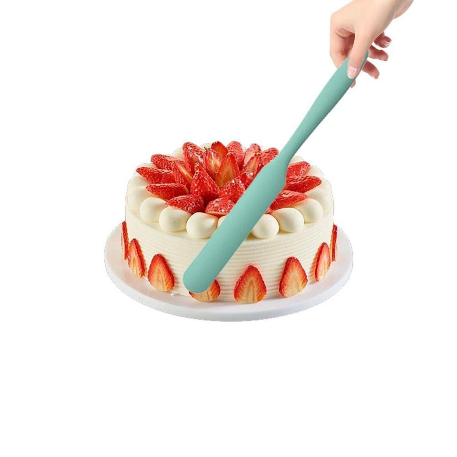 Eine Hand legt einen mintgrünen Tortenheber auf einen mit Erdbeeren bestrichenen, glasierten Kuchen auf einem weißen Teller.