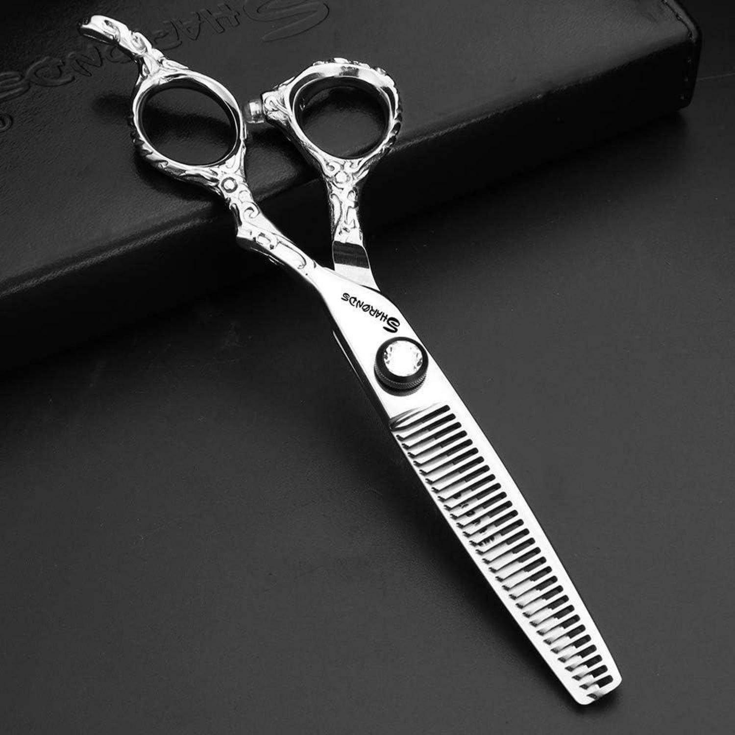Haarschneideschere aus Silber mit dünner Klinge, ornamentalen Fingerschlaufen und kammartiger unterer Klinge, gezeigt auf dunkler Oberfläche