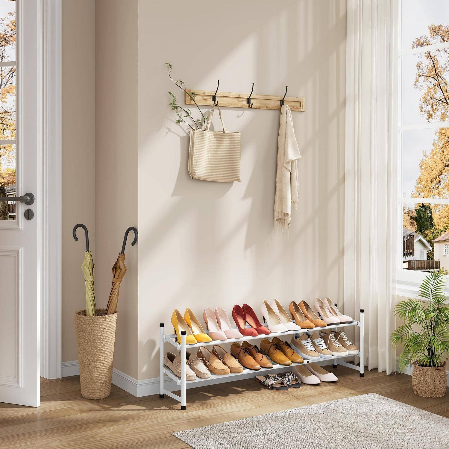 Heller Eingangsbereich mit einem Wandhaken, Regenschirmständer und einem zweistufigen Schuhregal, ordentlich organisiert mit Schuhen und Handtaschen, neben einem Fenster und einer Pflanze.