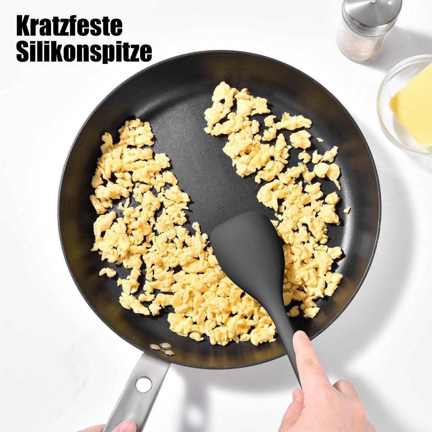 Schwarze Antihaft-Bratpfanne mit Rühreiern, die mit einem Silikonspatel gerührt werden; deutscher Text liest sich als „Kratzfeste Silikonspitze
