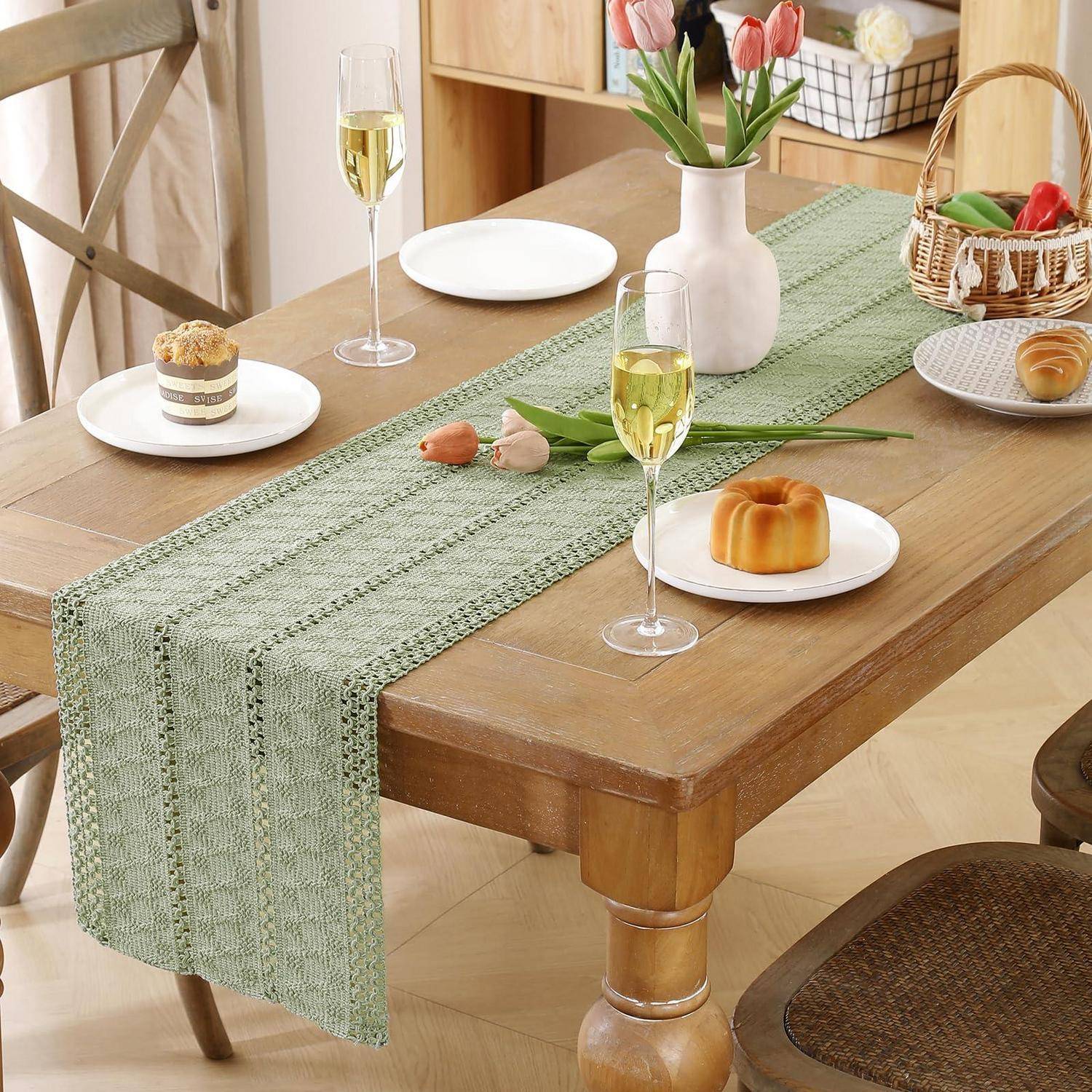 Tisch eindecken mit einem grünen Tischläufer, weißen Tellern, Gebäck, Champagnergläsern und einer Vase mit Tulpen in einem hellen Raum.