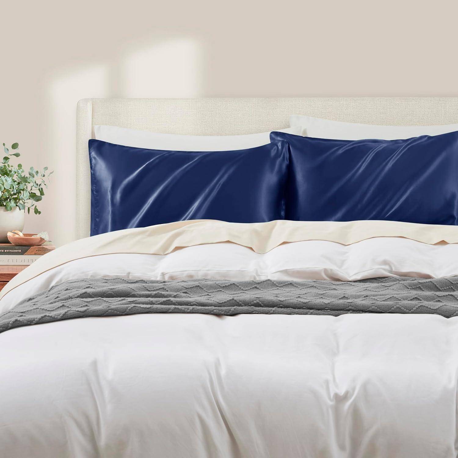 Ein ordentlich gemachtes Bett mit weißen Laken, einer grauen Steppdecke und zwei dunkelblauem Kissen gegen ein hell gepolstertes Kopfteil.