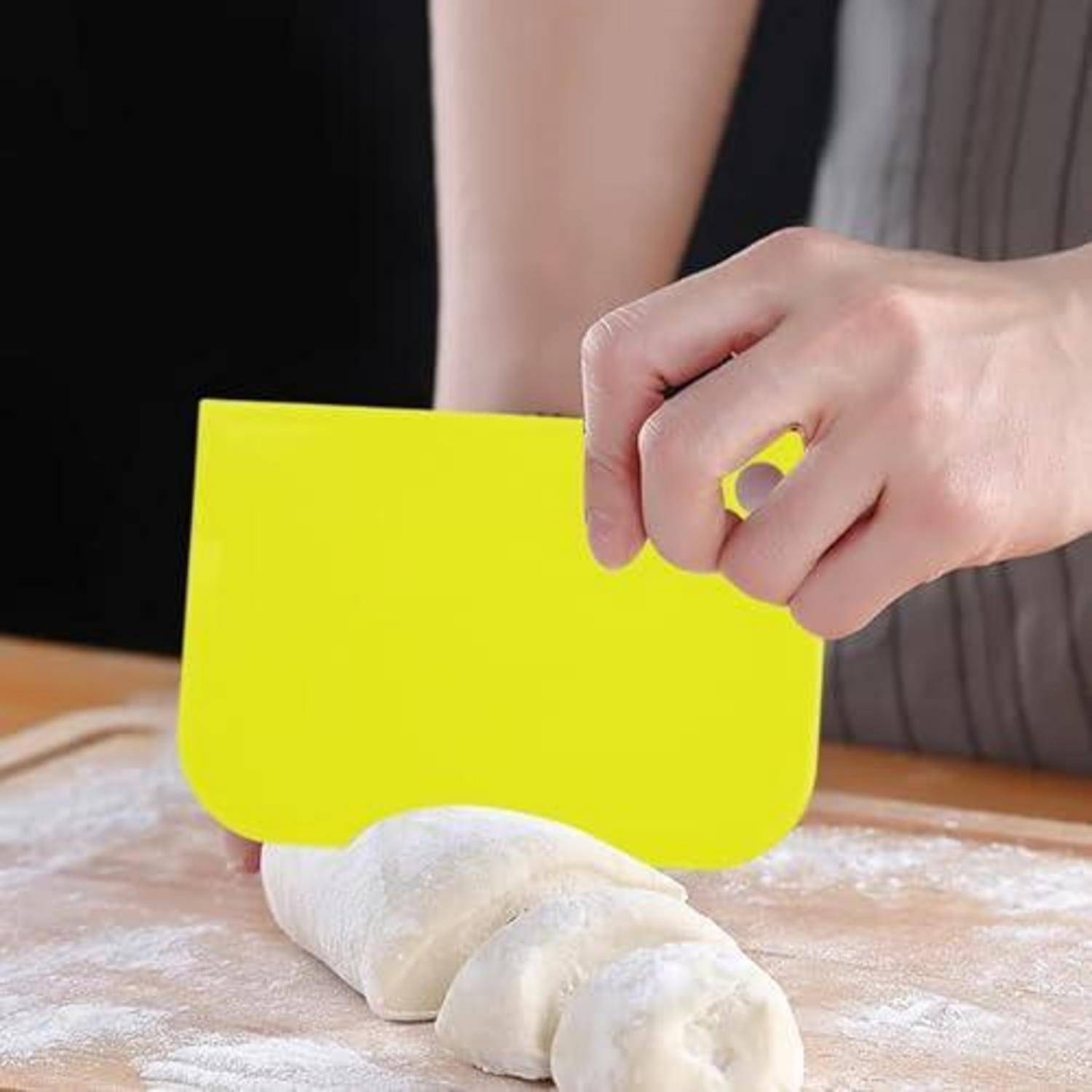 Hand, die einen gelben Teigschaber verwendet, um bemehlten Teig auf einem Holzbrett zu schneiden.