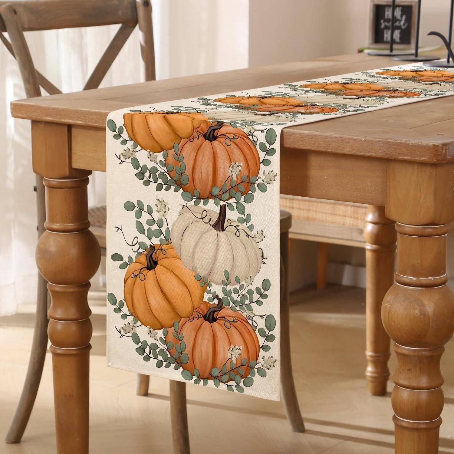 Herbst-Tischläufer mit bemalten Kürbissen und grünen Blättern, drapiert über einen Holzspeisetisc und Stuhl.