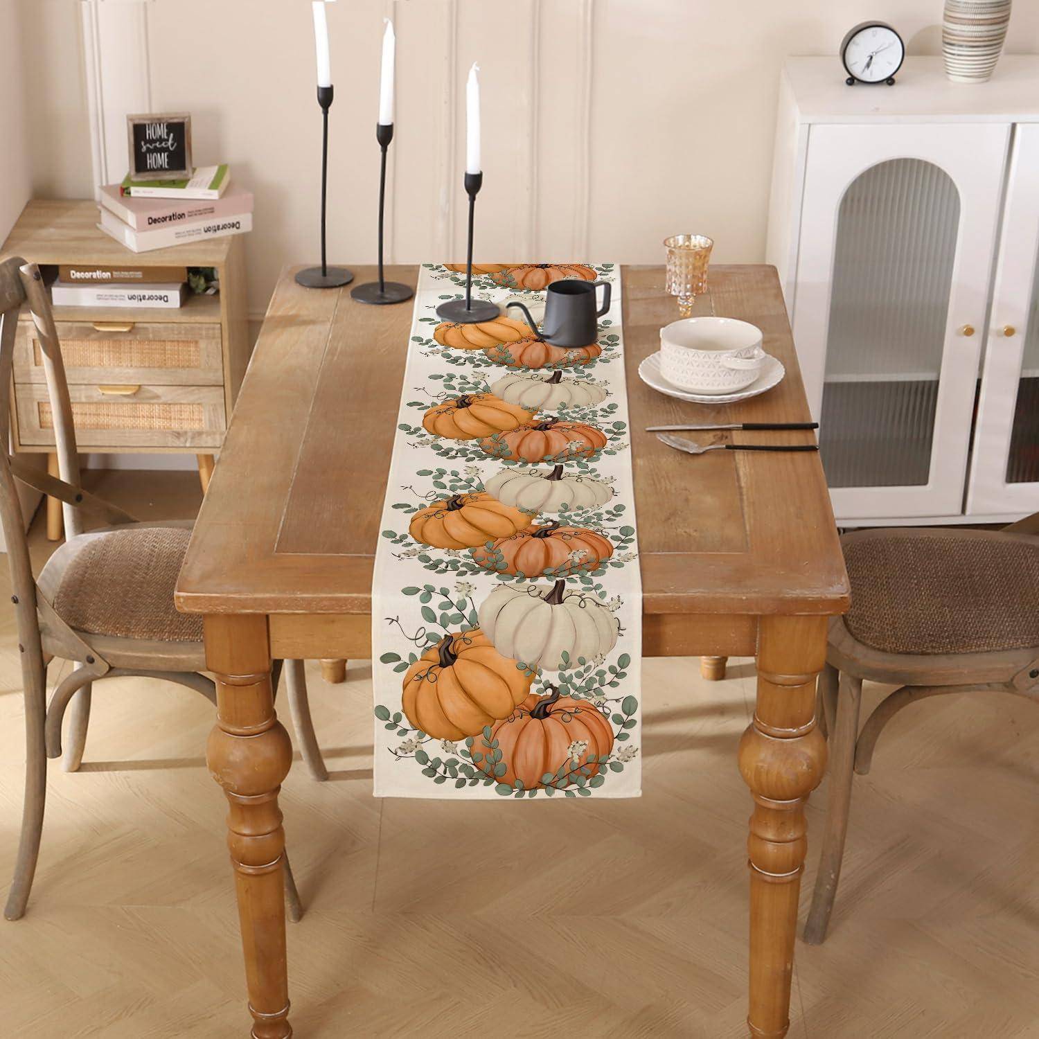 Kürbis-themed Tischdeckung auf einem Holzesstisch mit Stühlen, Kerzen, gestapeltem Geschirr und Herbstdekoration in einem gemütlichen Zimmer.