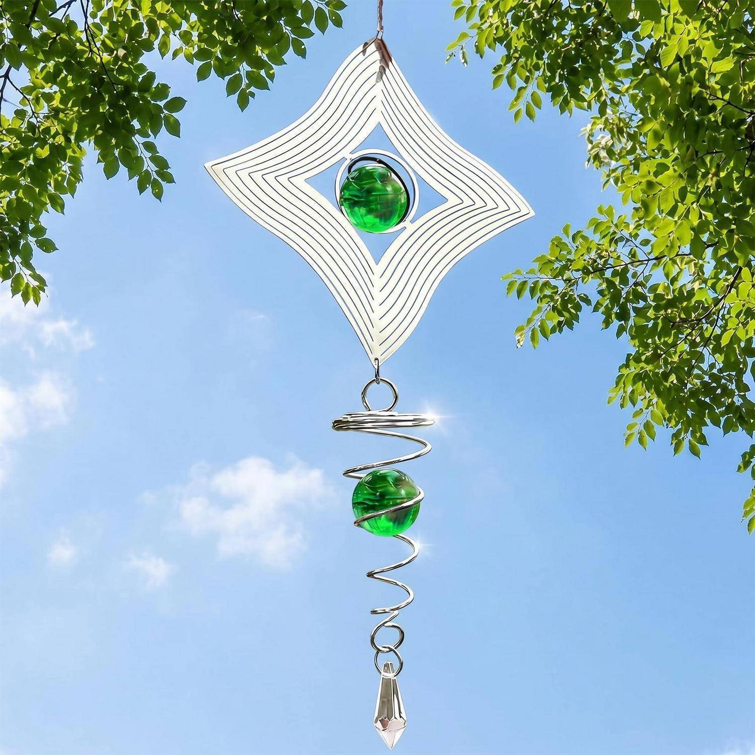 Dekorativer Windspiel mit weißem Diamantrahmen, grünen Glasperlen und einem Kristall, der gegen einen blauen Himmel und Baumblätter hängt.