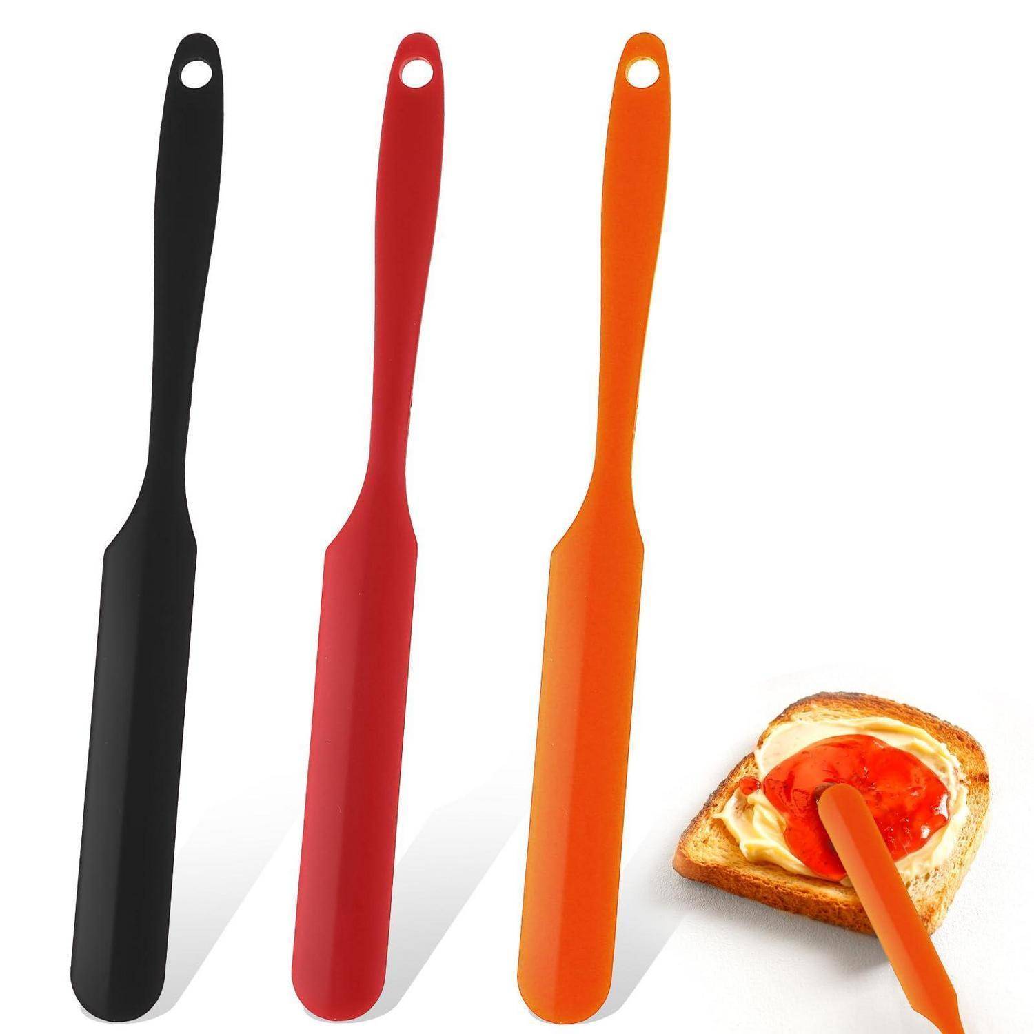 Drei Silikonspachtel in Schwarz, Rot und Orange neben einer Toastscheibe mit aufgestrichener Creme.
