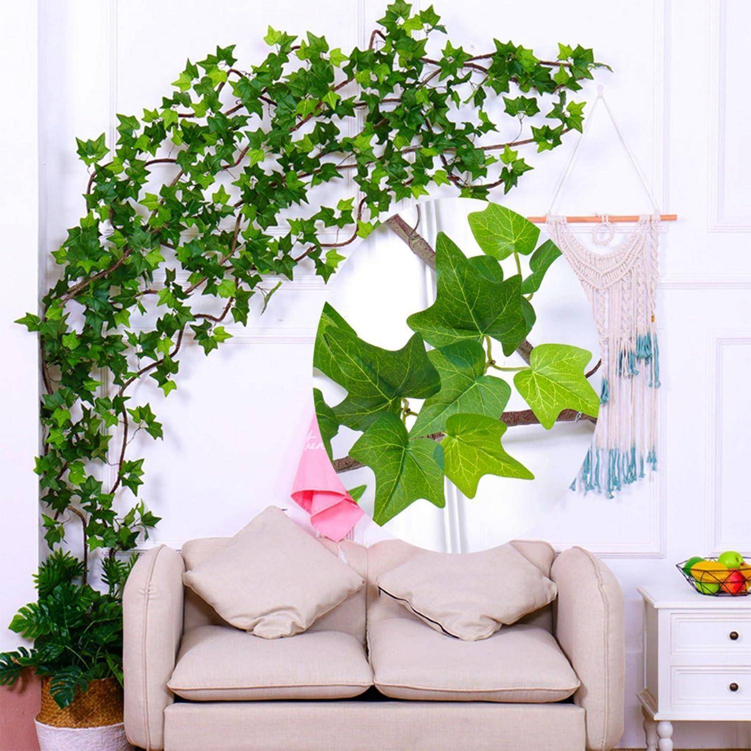 Wohnzimmer mit beigem Sofa unter einer efeubedeckten Astdeko, großen grünen Blättern, die an der Wand hängen, und einer Makramee-Wanddekoration auf der rechten Seite.