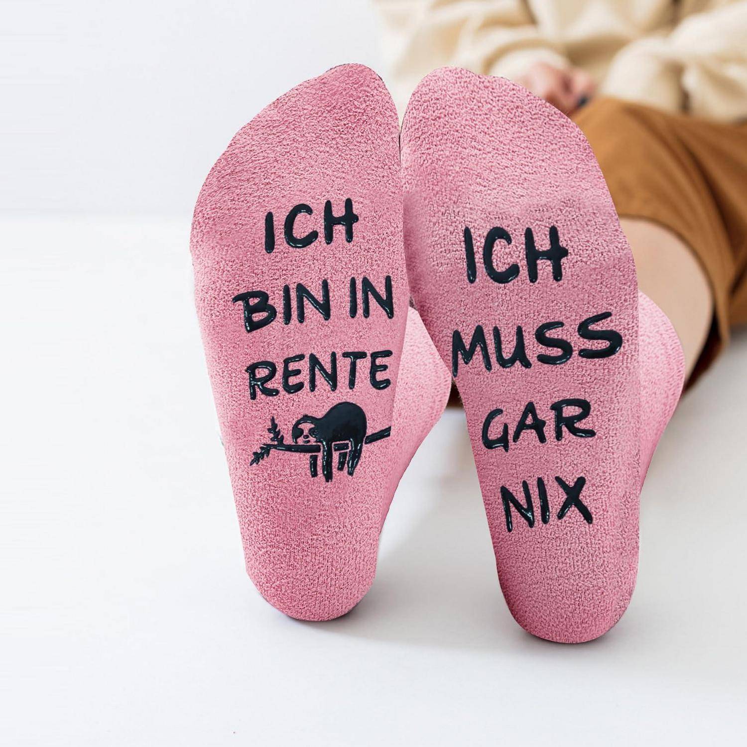 Nahaufnahme von Füßen in rosa Socken mit deutschem Text: 'ICH BIN IN RENTE' und 'ICH MUSS GAR NIX', was bedeutet, dass man in Rente ist und keine Verpflichtungen hat.