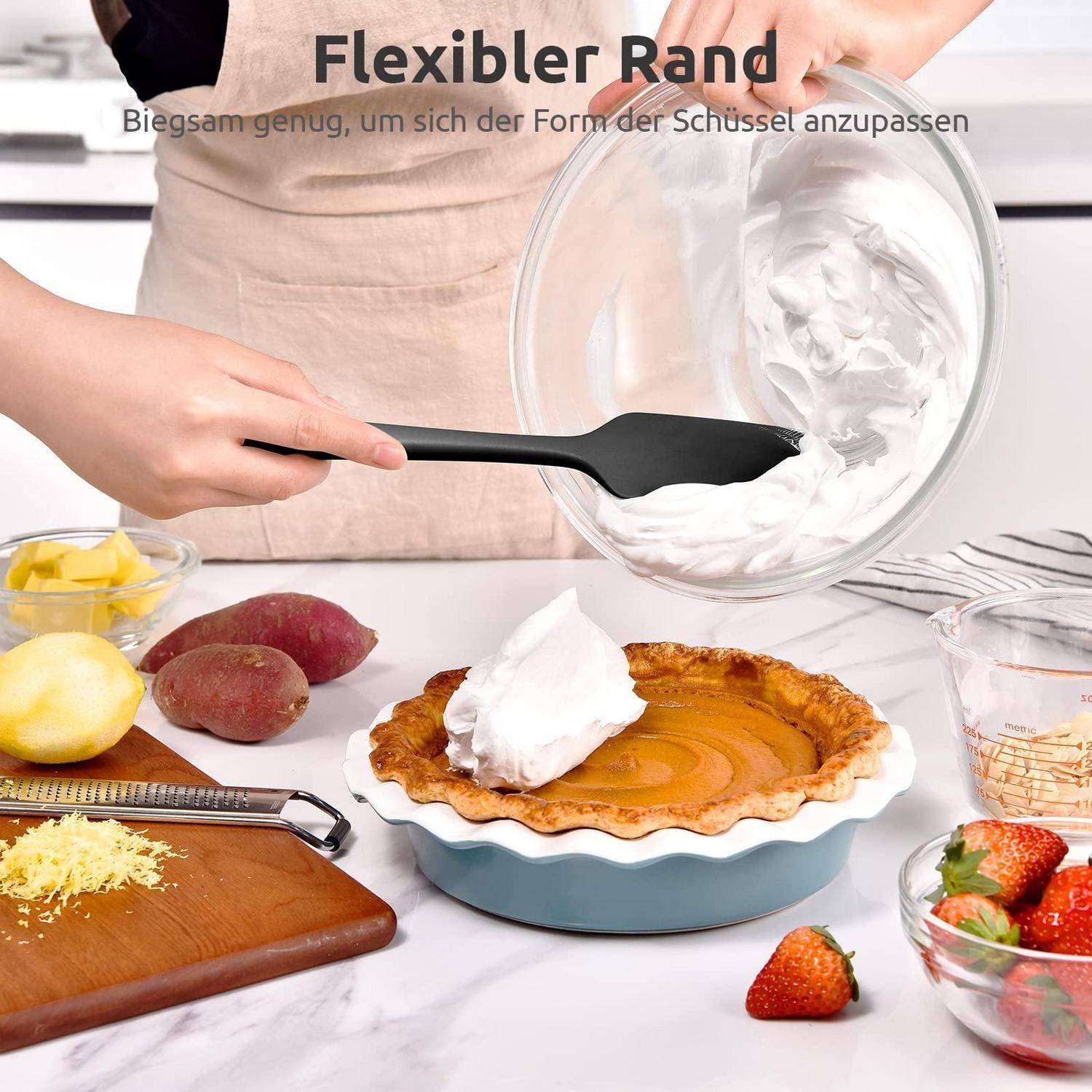 Person mit einem flexiblen schwarzen Spatel, der Schlagsahne aus einer Glassschüssel auf einen Kuchen kratzt, mit Obst und Backutensilien auf einer Küchentheke; Text sagt 